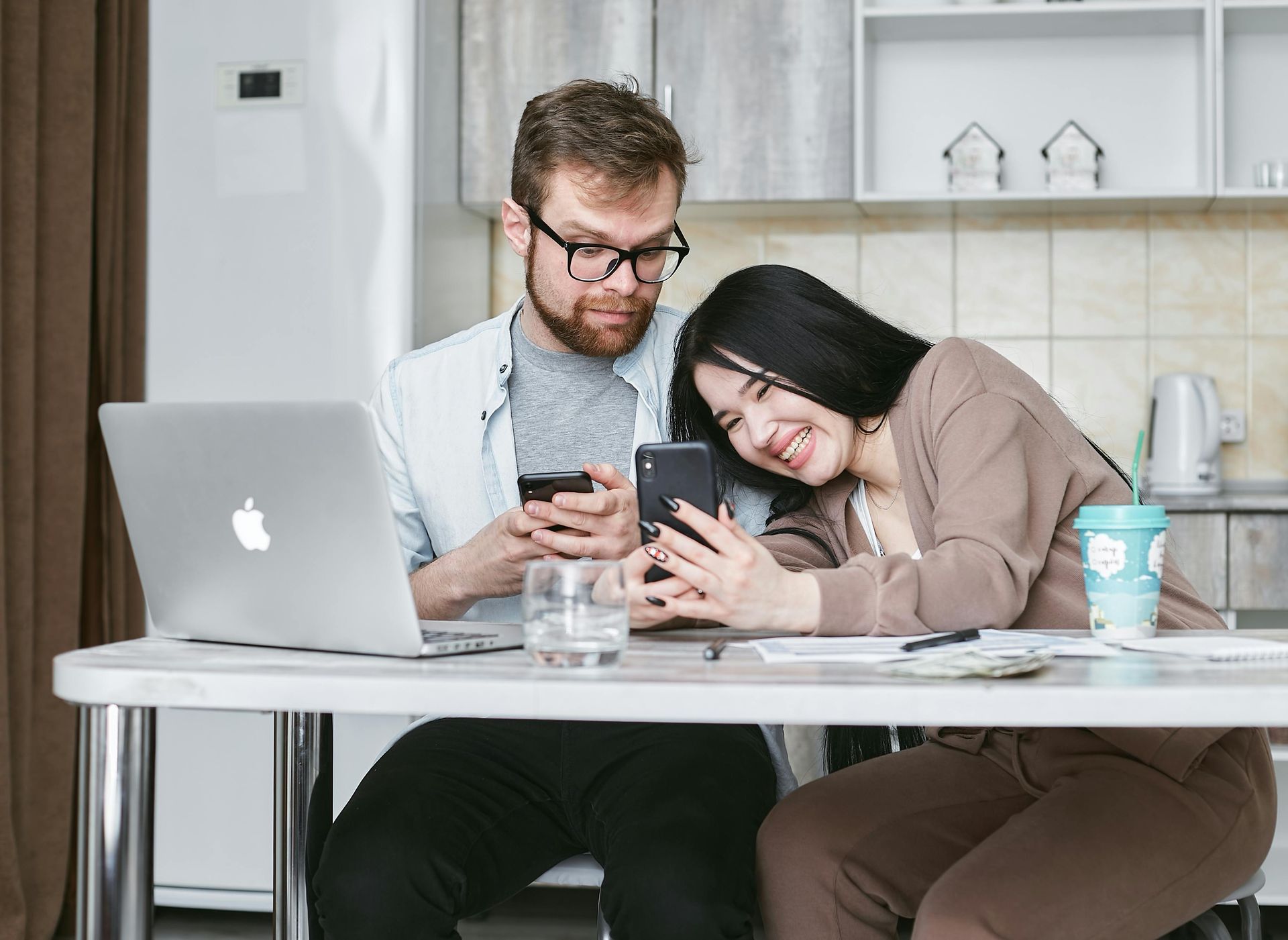 A man and a woman are looking at a laptop computer in a kitchen.