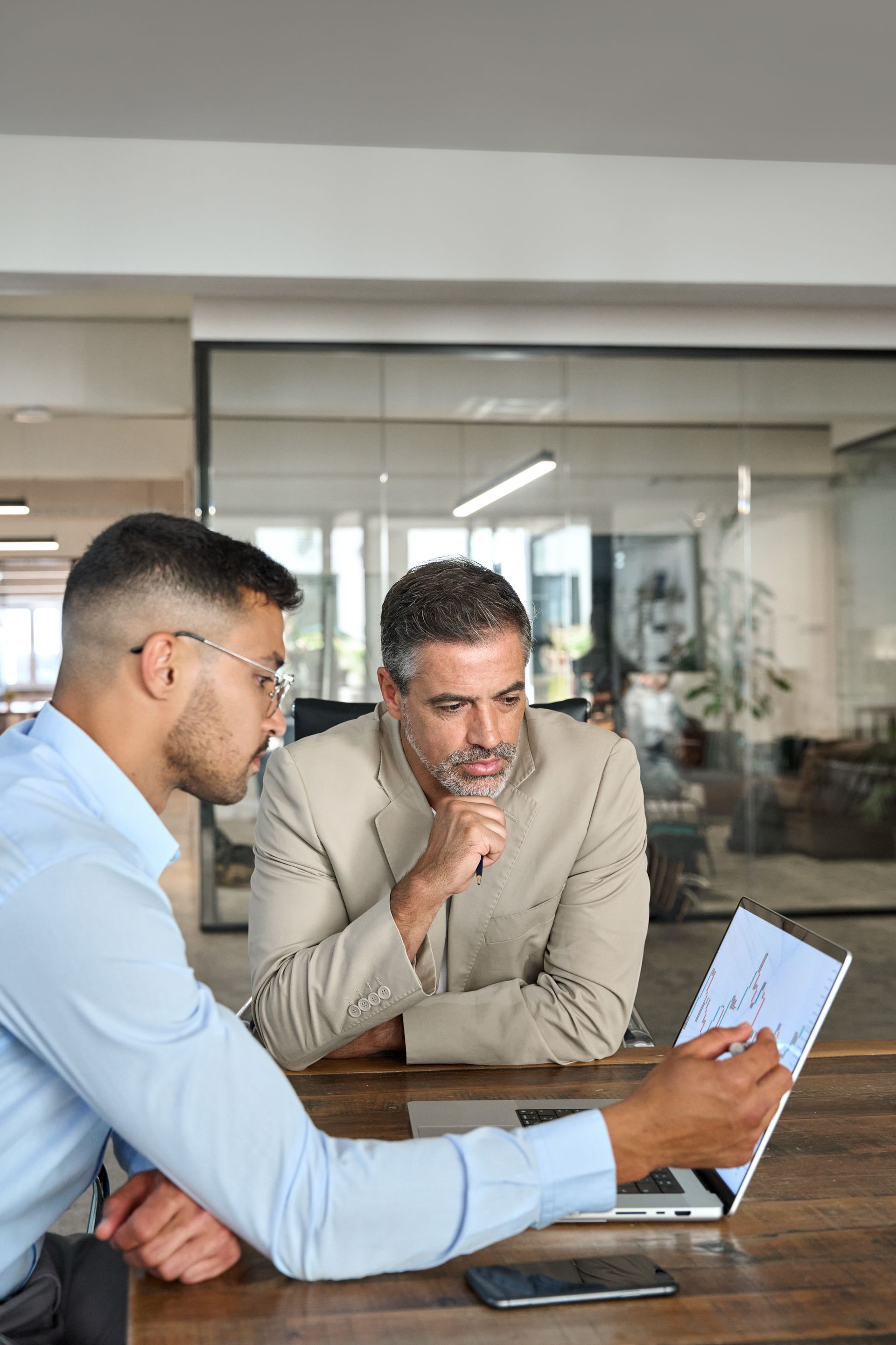Two men are sitting at a table looking at a laptop.