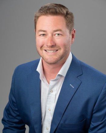 A man in a blue suit and white shirt is smiling for the camera.