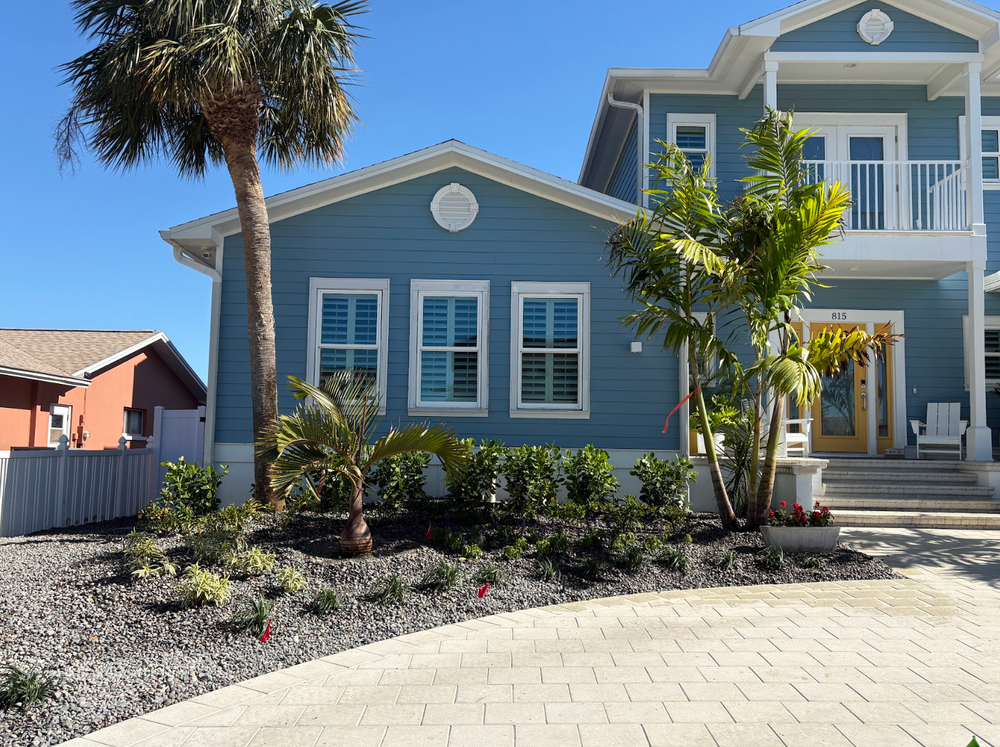 Blue house with white trim and palm trees in a tropical setting. Gravel landscaping and paved driveway.