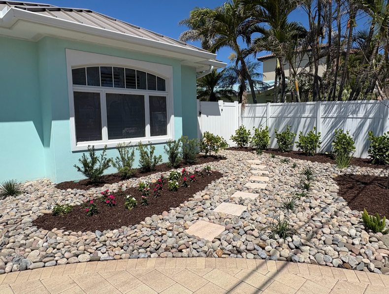 A light blue house with a landscaped yard. A pathway made of square stones leads to the door.