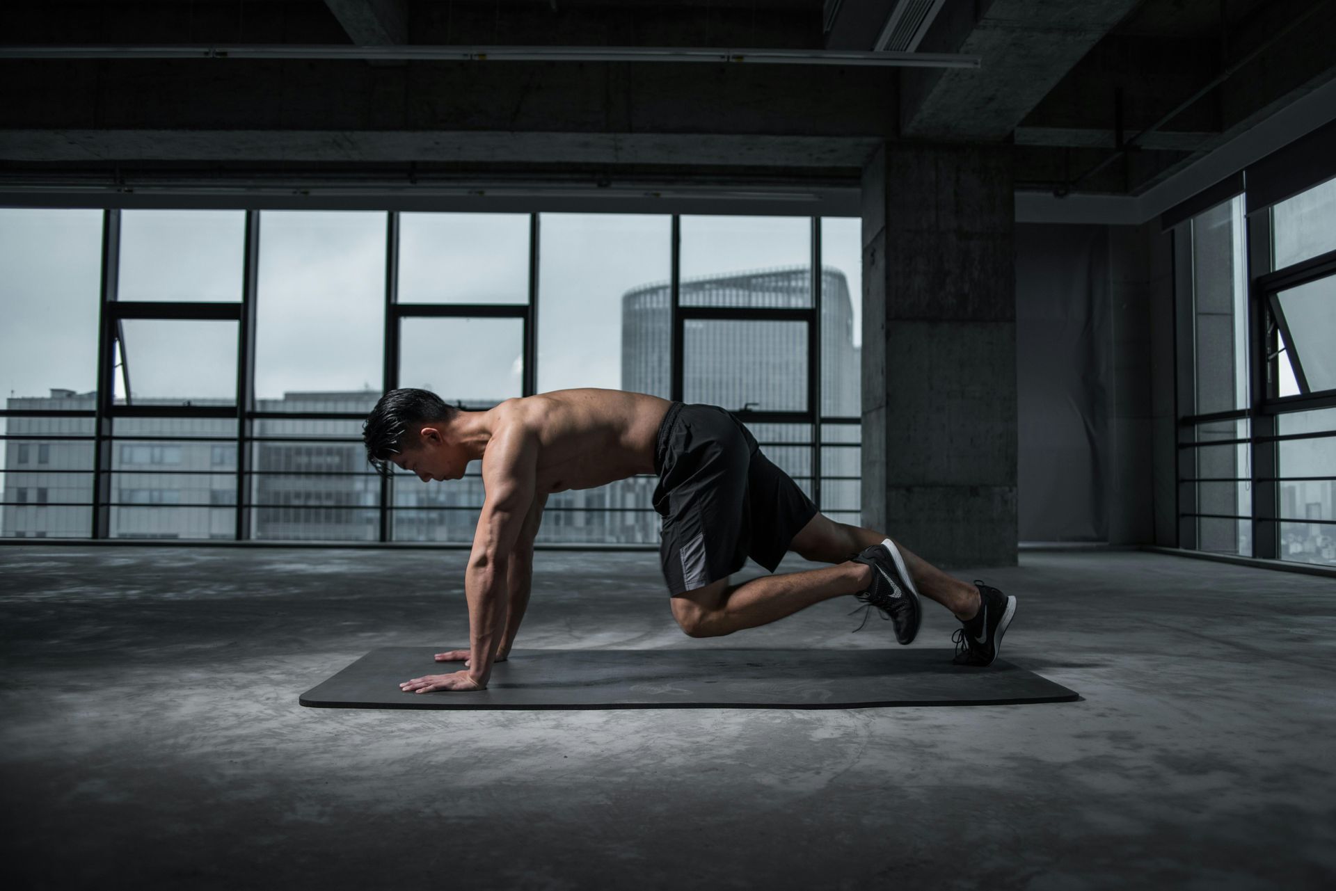 Man doing mountain climber exercise on a mat, in a dark, urban gym.