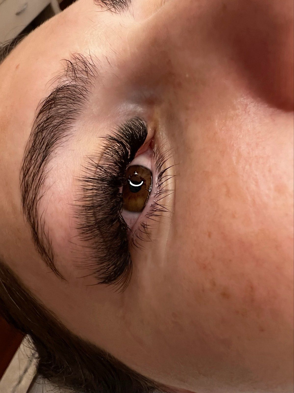 Close-up of a person's eye with thick, dark eyelash extensions and a well-groomed eyebrow.