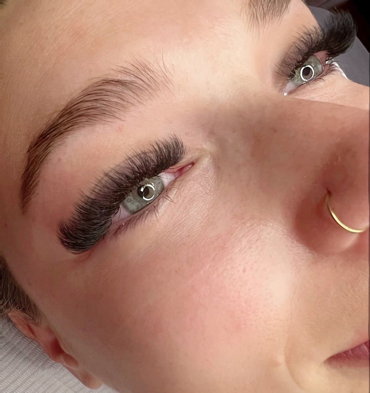 Close-up of a person with full, dark eyelash extensions and a gold nose ring.