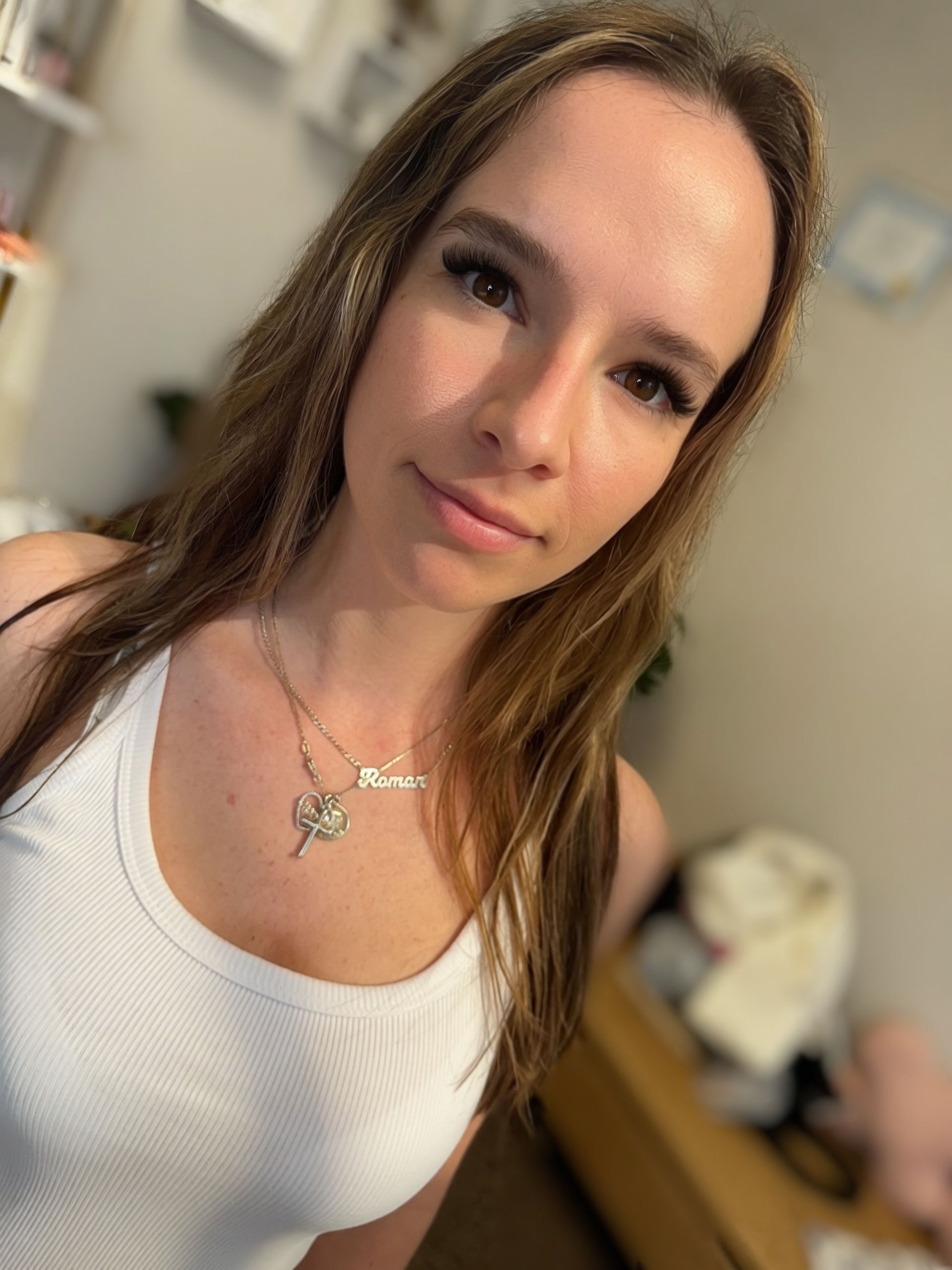 Woman in white tank top, looking at the camera, with a necklace.