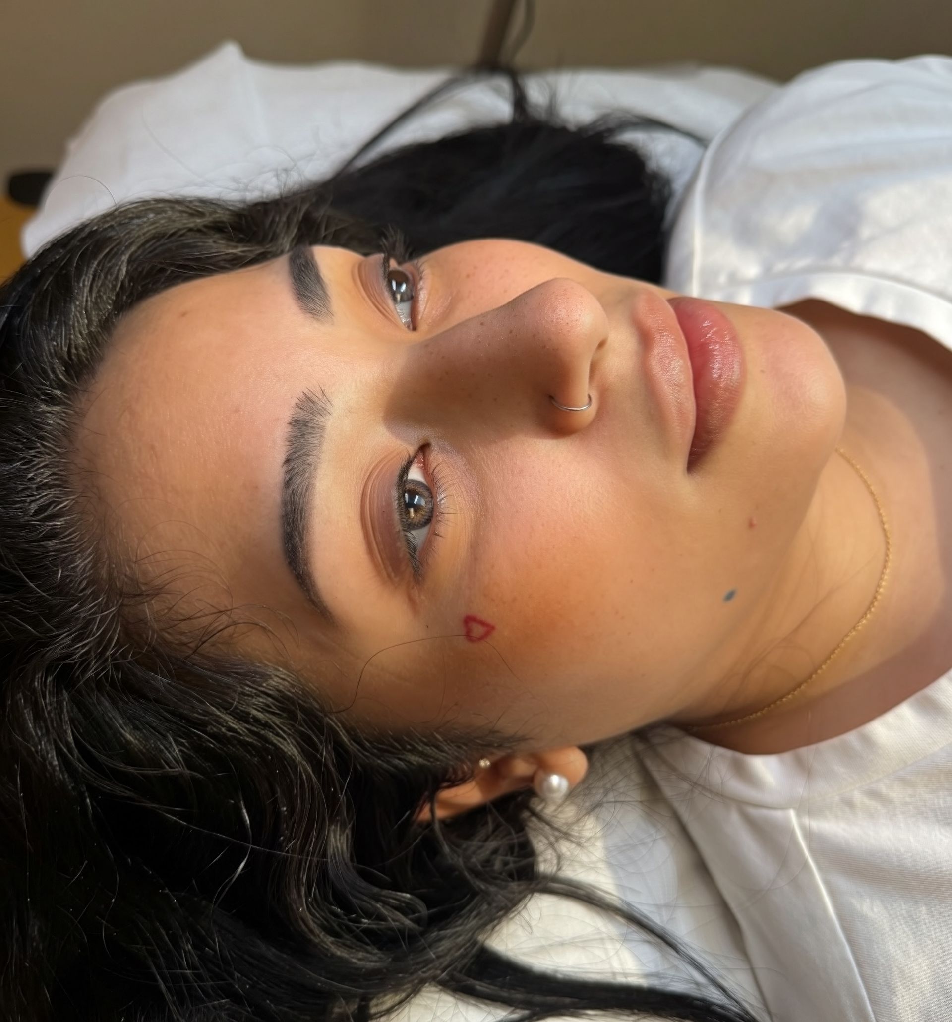 Woman with dark hair and a heart tattoo on her cheek; looking at the camera.