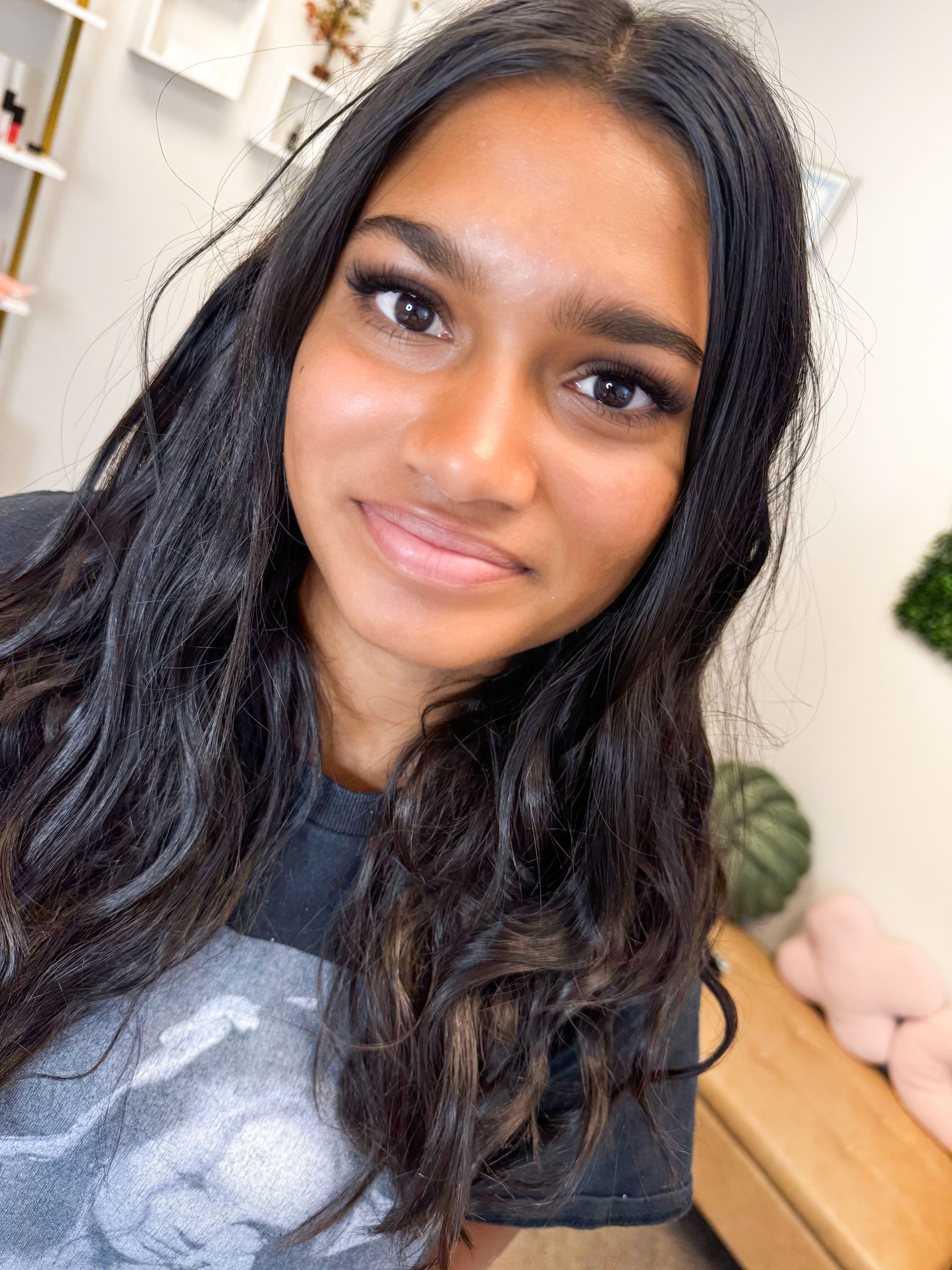 Young person with long dark hair smiles at the camera. They are in a well-lit indoor setting.