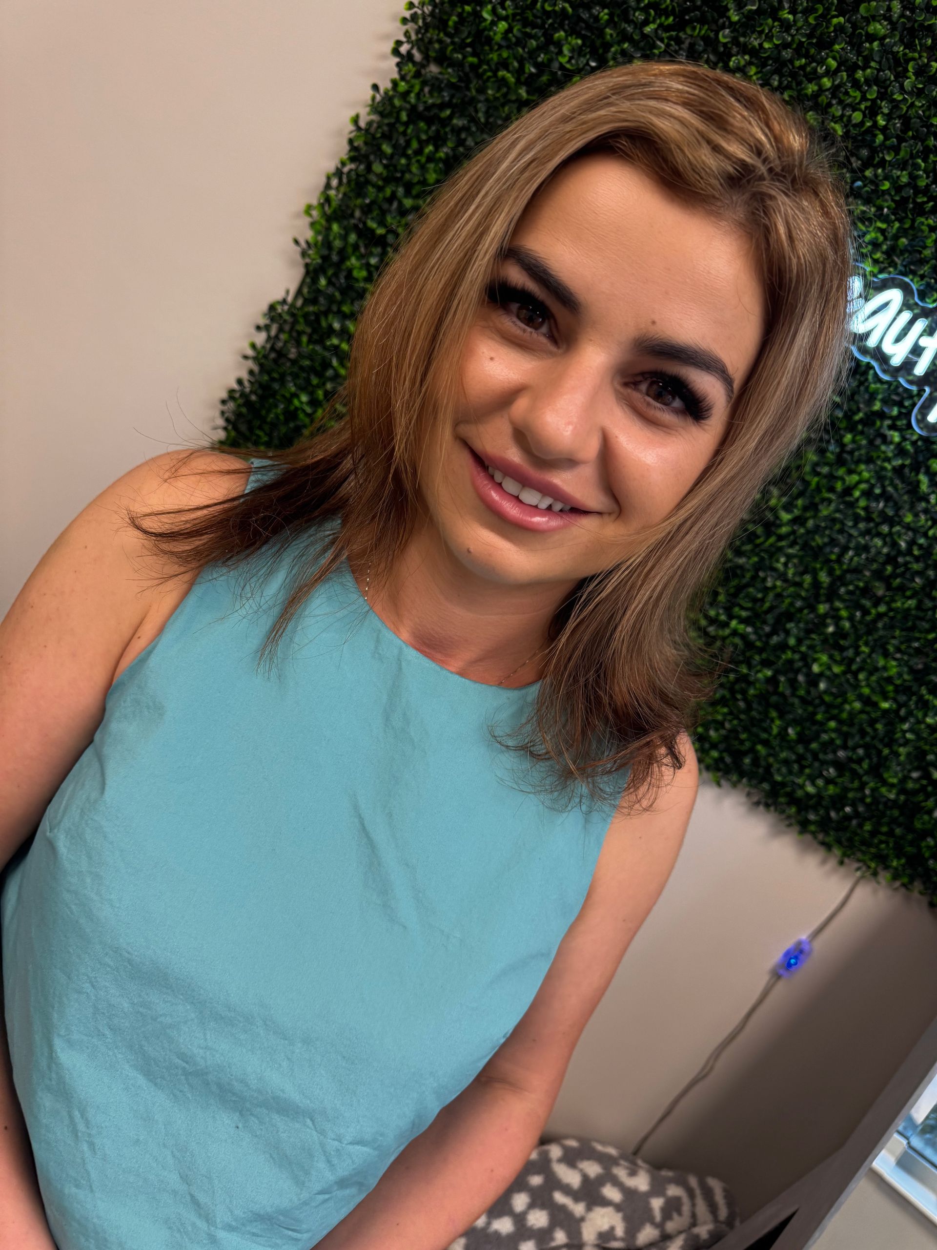 Woman in teal top smiles in front of green wall.