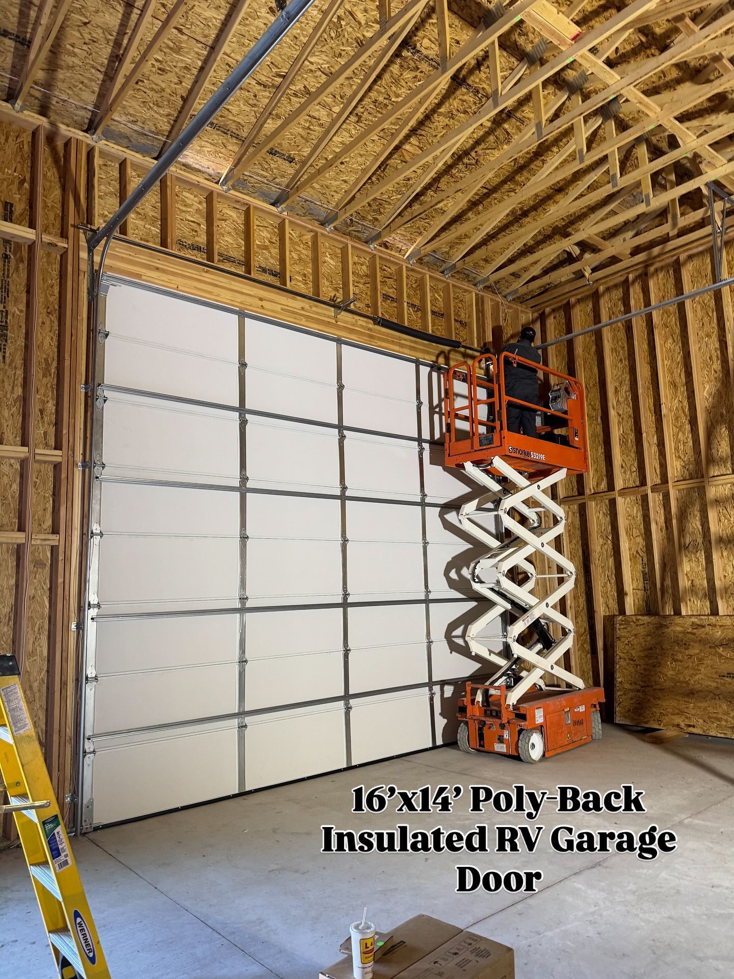 A 16'x14' RV garage door is installed inside a wooden structure. A scissor lift is positioned next to the door.
