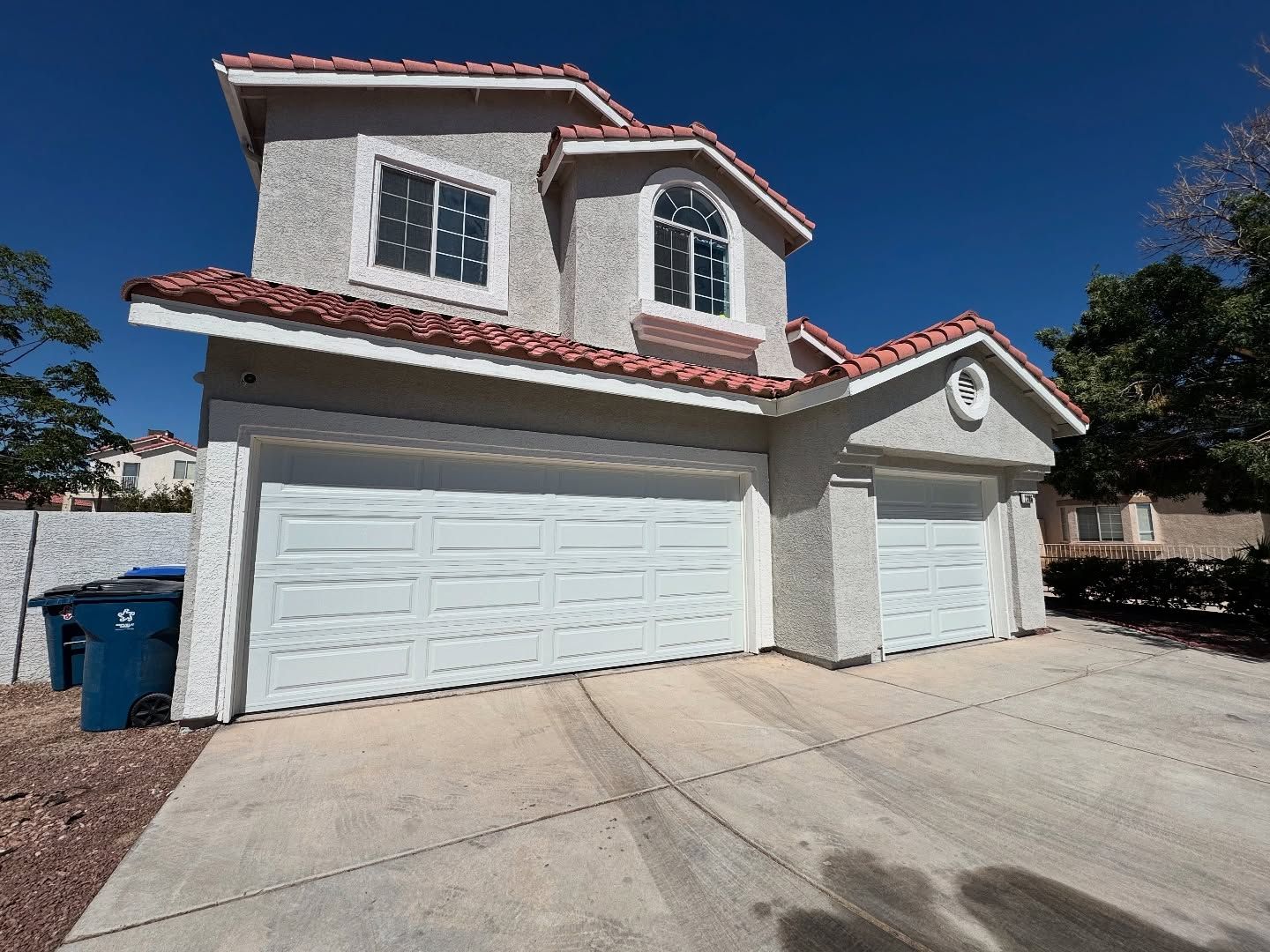 Two-story stucco house with red-tiled roof and two-car garage under a clear blue sky.