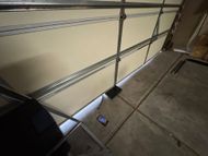 Garage interior with a partially open door, metal track, and a black box on the floor.