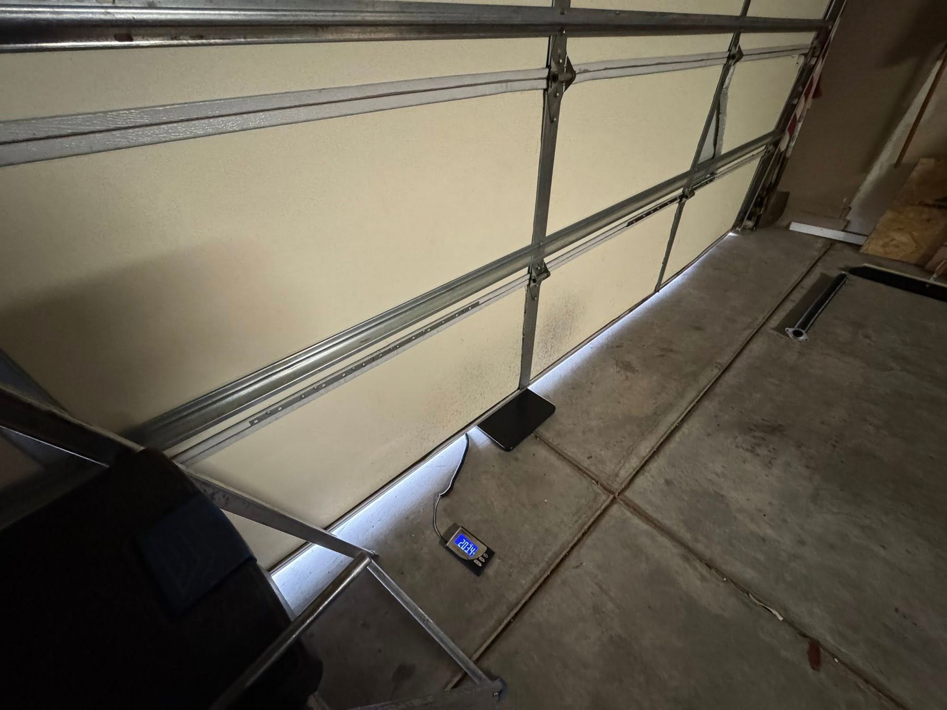 Garage interior with a partially open door, metal track, and a black box on the floor.