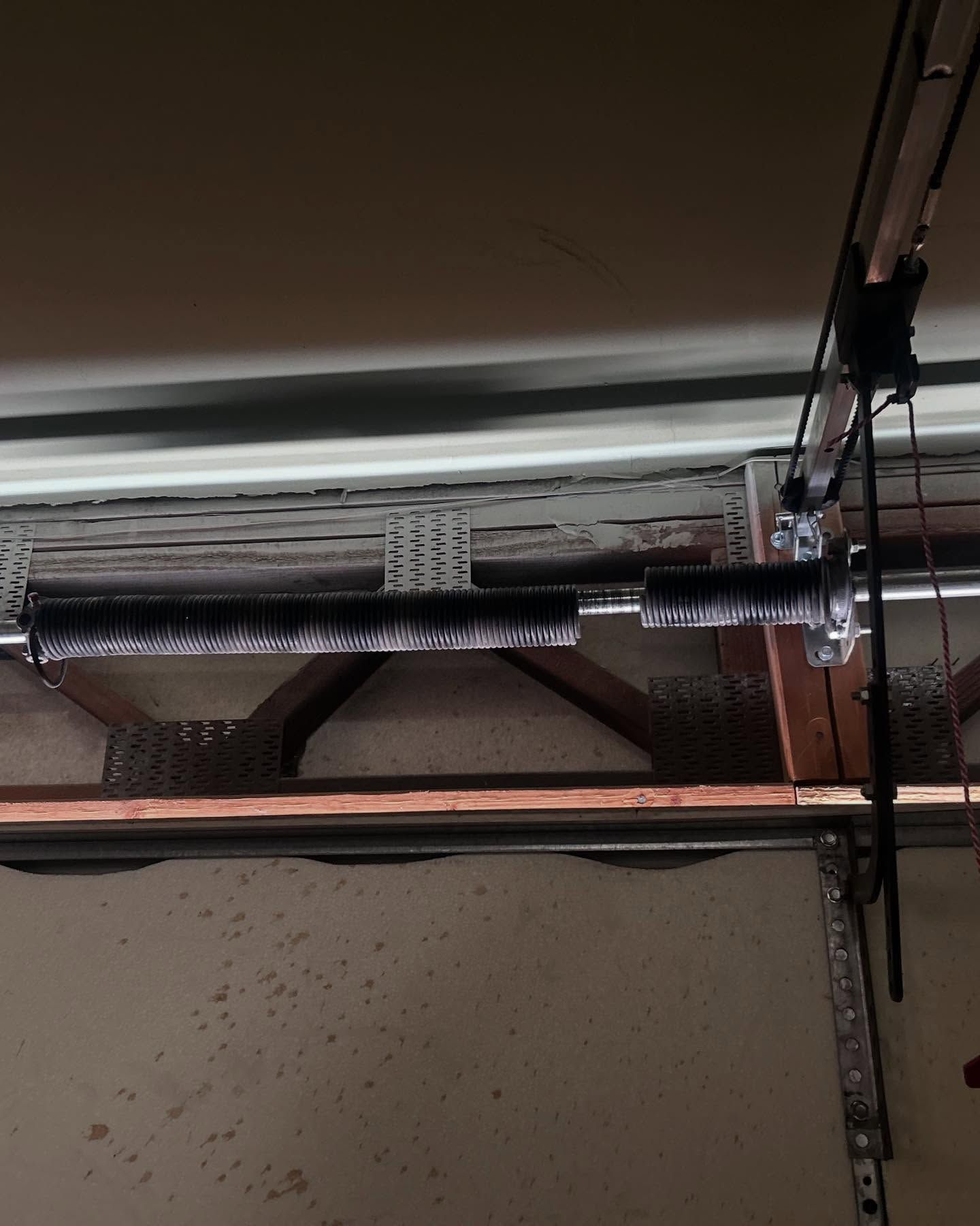 Garage door torsion spring, coiled, with a broken section visible, mounted overhead.