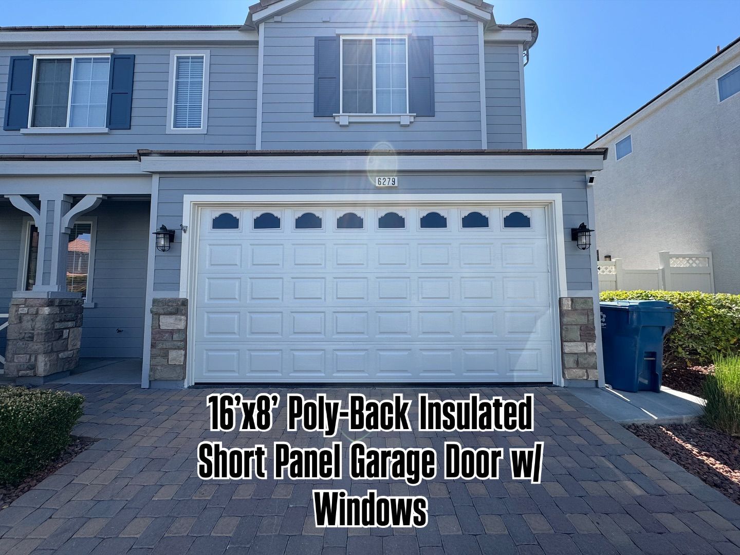 Exterior of a two-story house with a white 16'x8' garage door with windows, on a brick paved driveway.