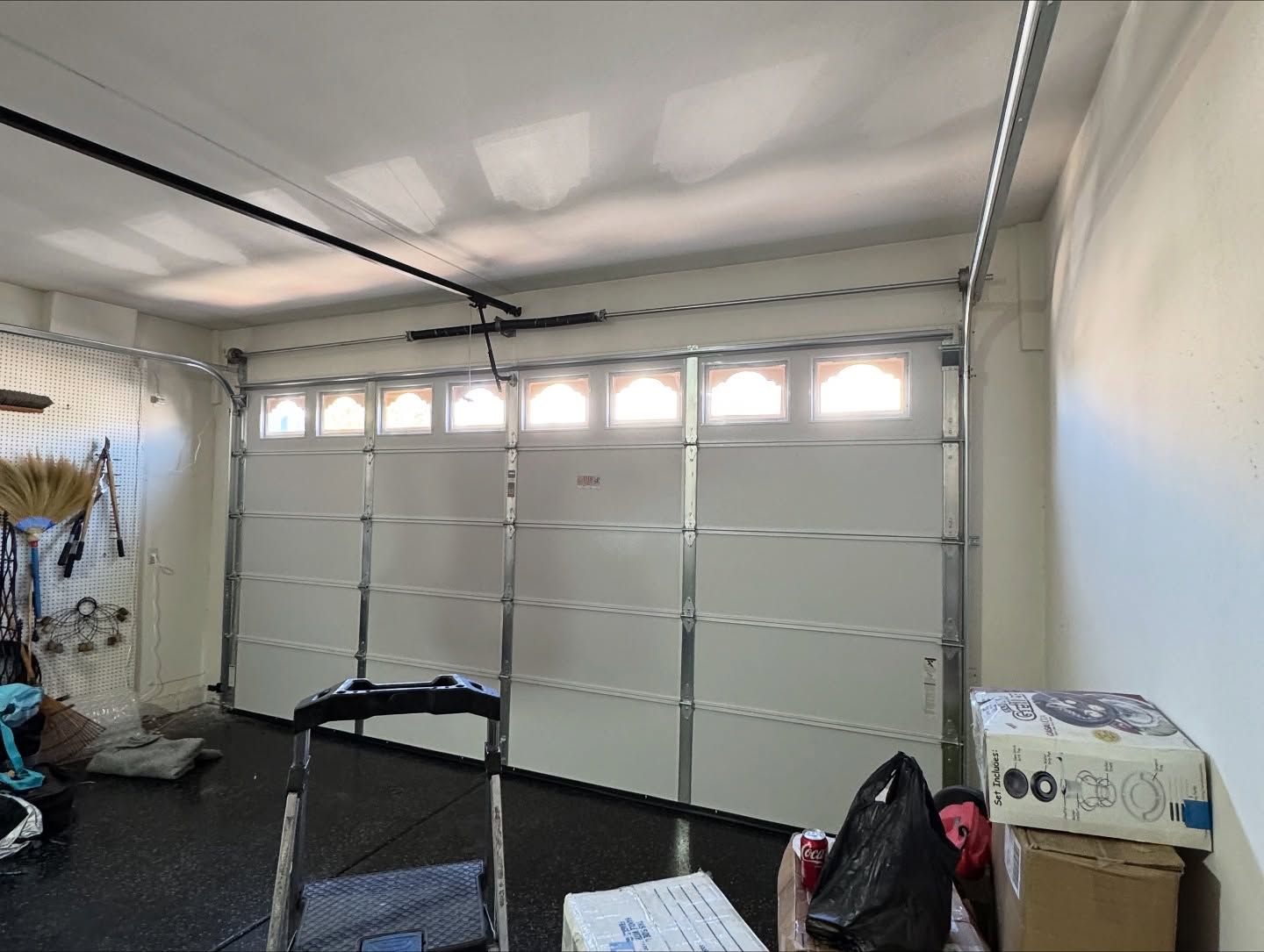 Garage door, white panels, windows across the top, inside a garage with equipment and boxes.
