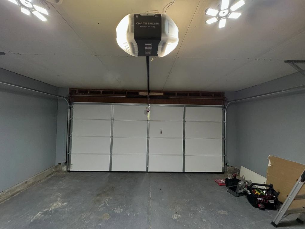 Interior view of a garage with a closed white garage door. A garage door opener is mounted on the ceiling.