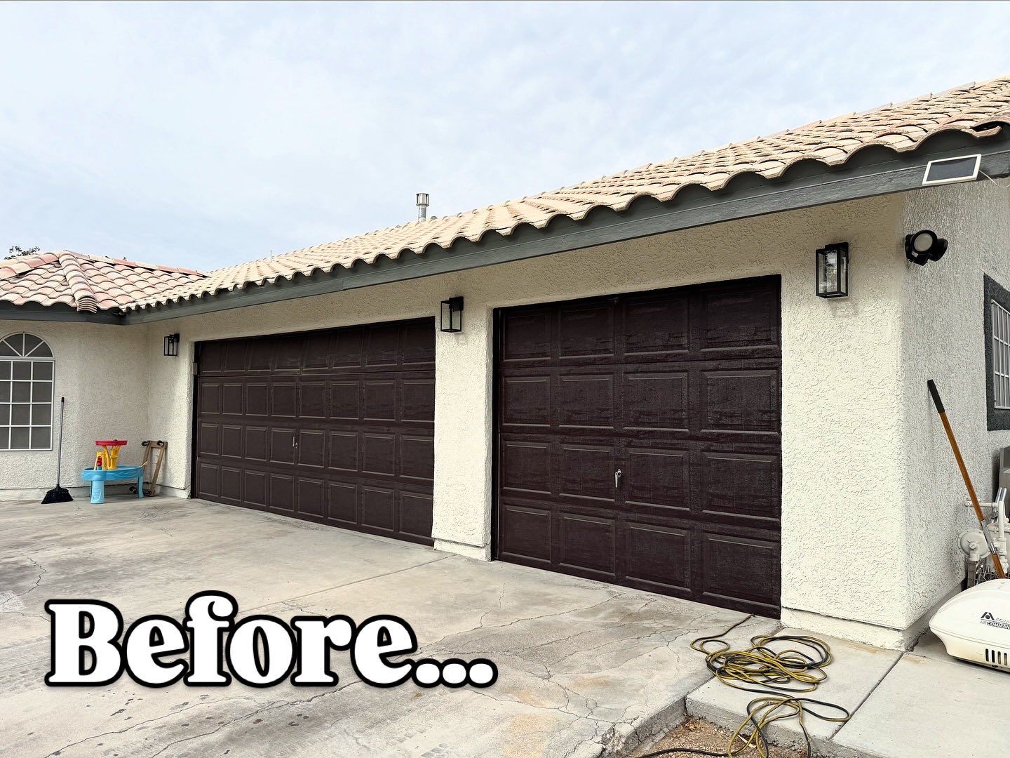 Garage with brown doors; cream-colored stucco siding, beige roof. 