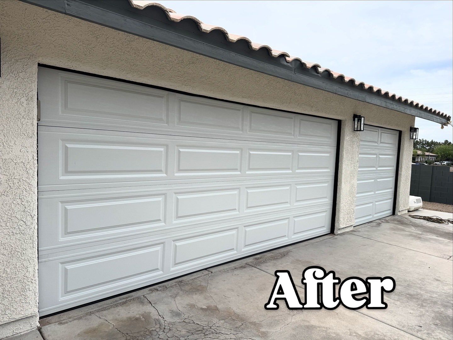White garage doors on a stucco building with a concrete driveway; 
