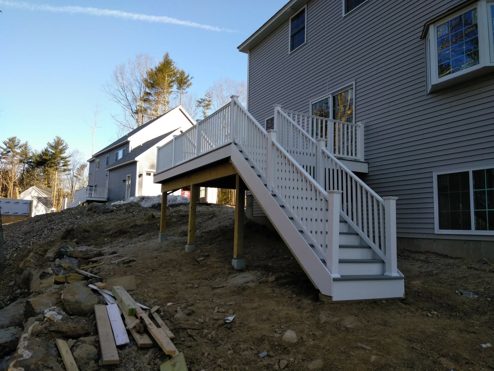 A white deck with stairs leading up to it in front of a house.