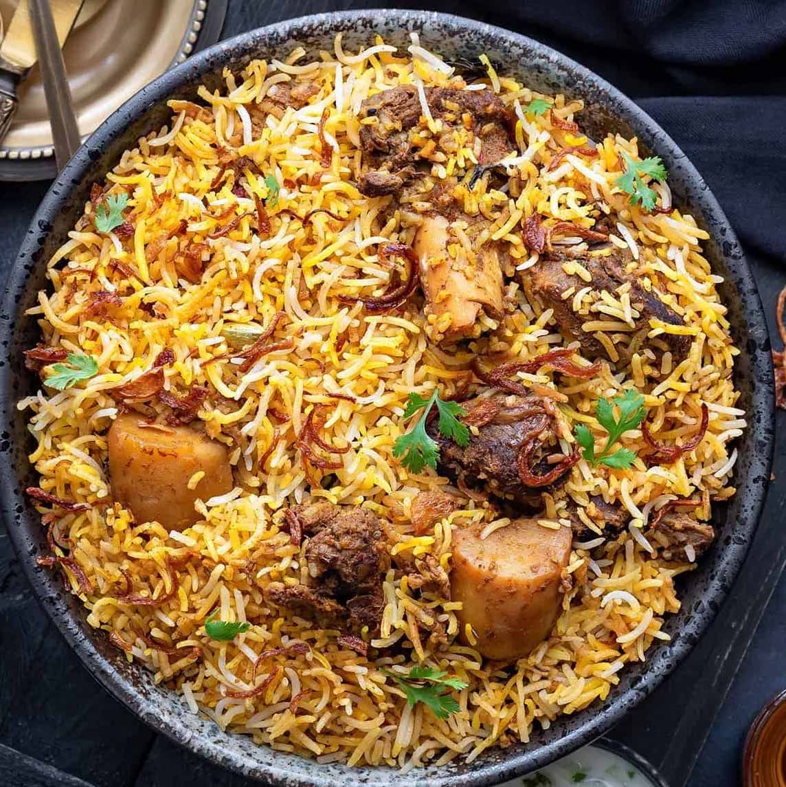 Un bol de biryani avec de la viande et des pommes de terre sur une table.