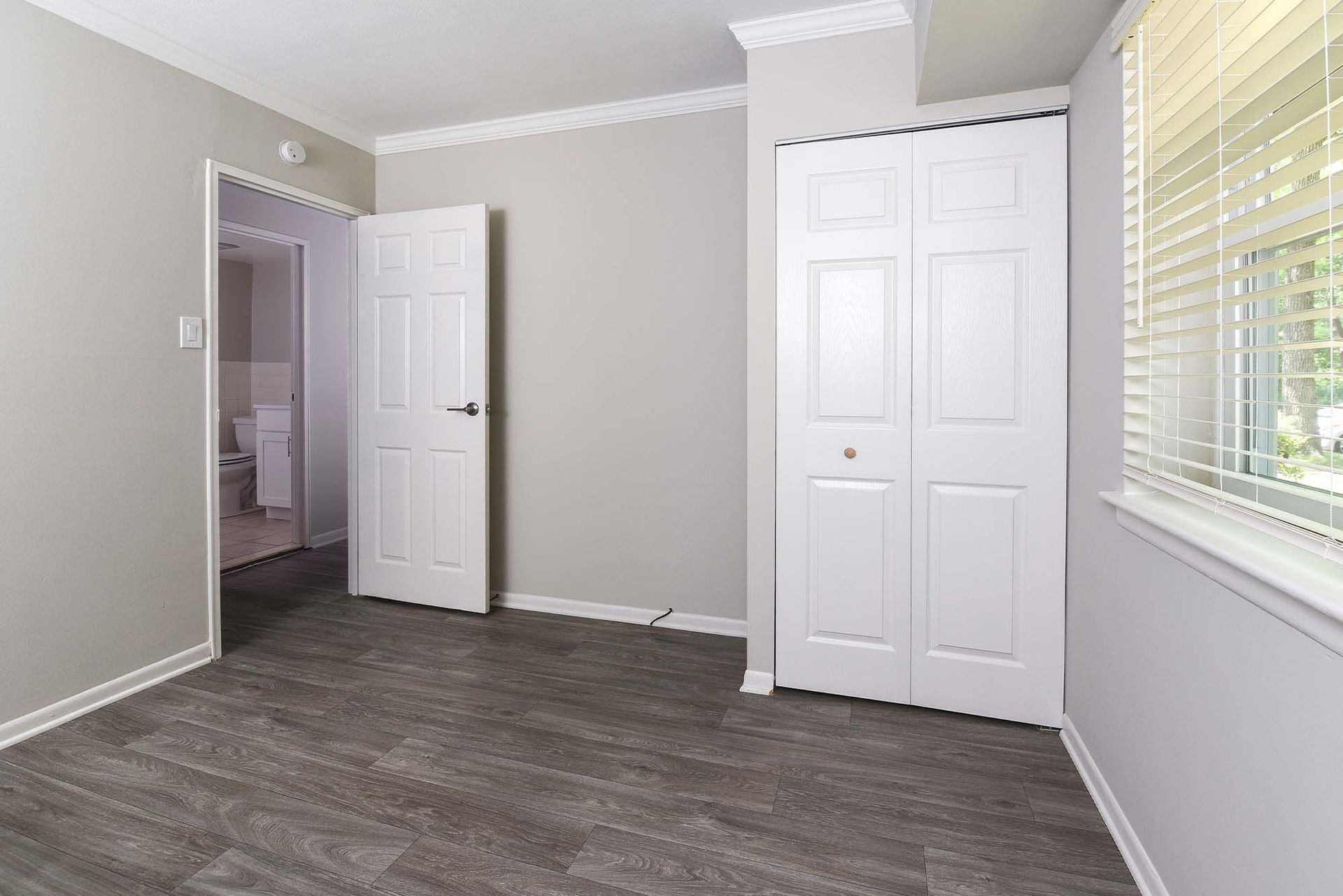 Bedroom with white closet doors, laminate flooring, and a window with blinds.
