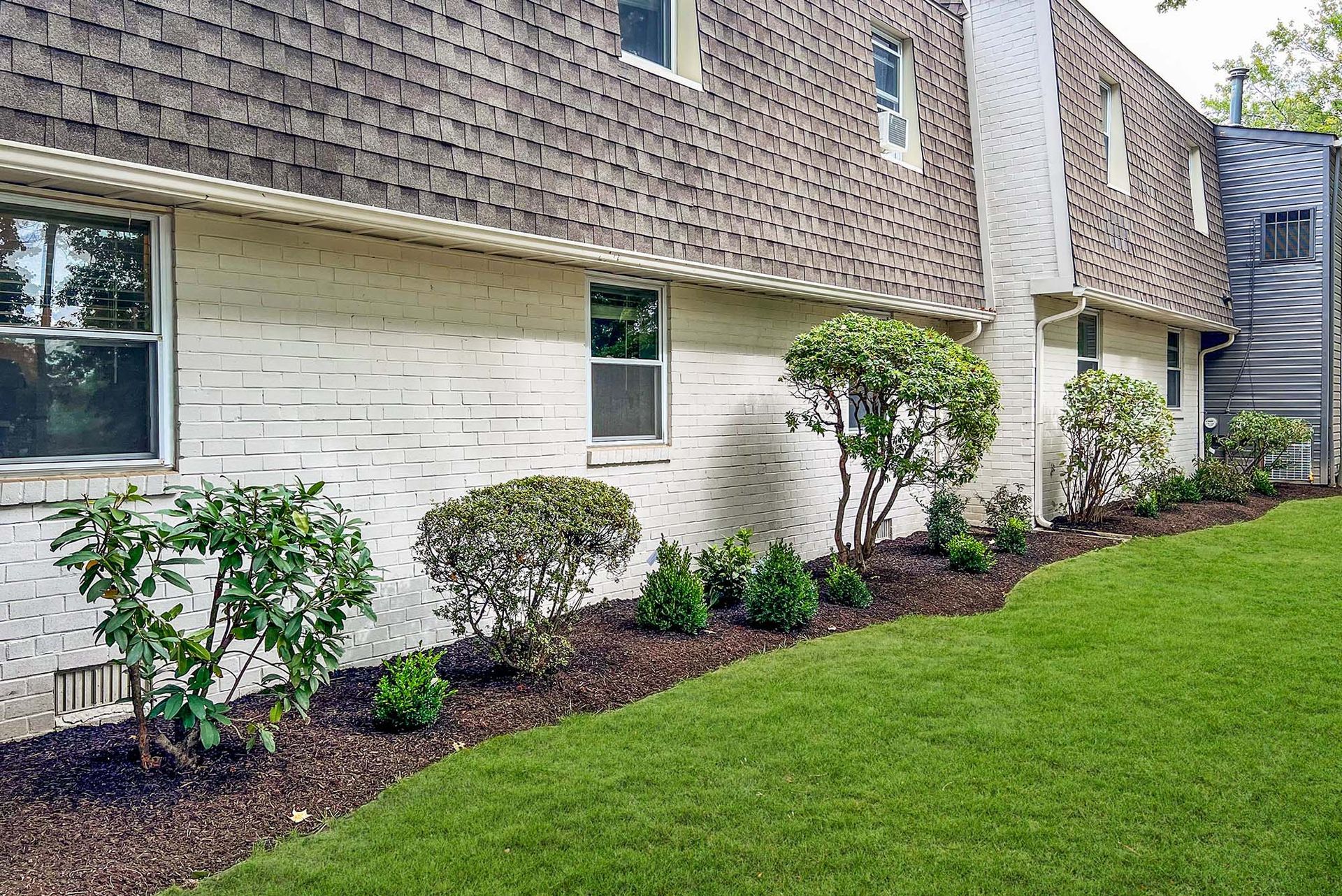 Exterior view of apartment building with white brick base, brown shingled upper facade, and landscaped lawn
