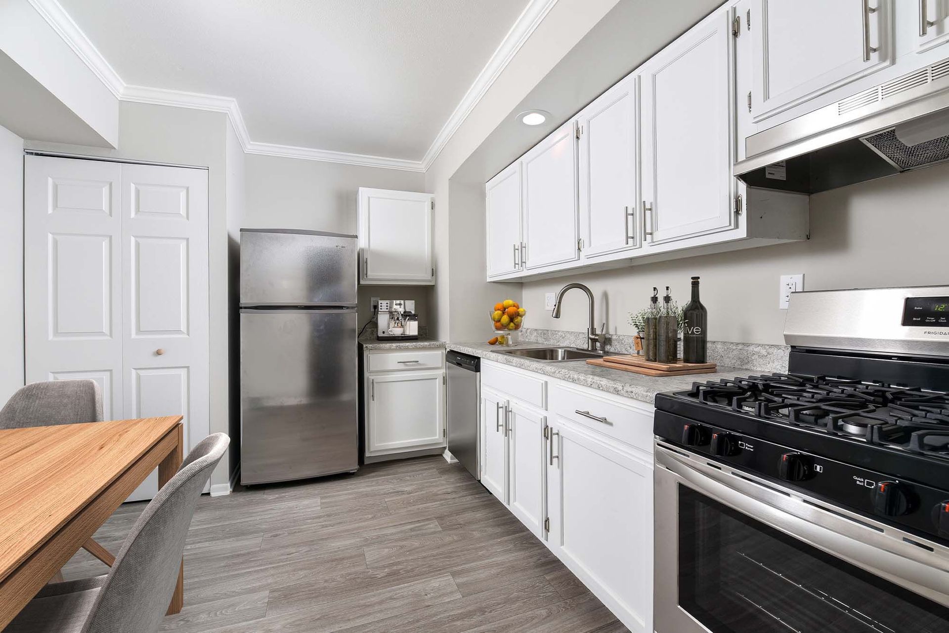 Modern apartment kitchen with white cabinets, stainless steel appliances, and a wooden dining table.