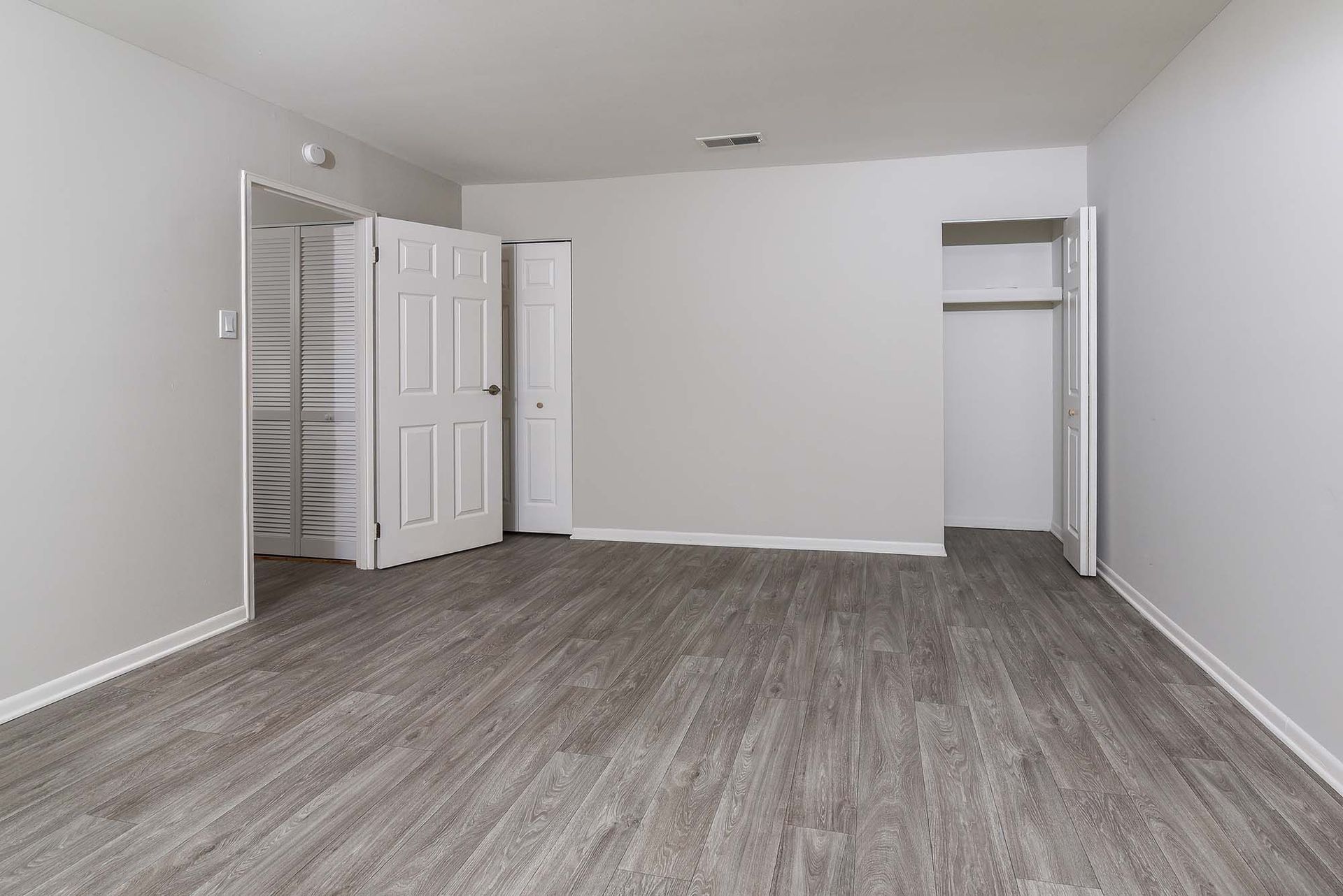 Empty living area with gray walls, white trim, wood-look flooring, and a closet.