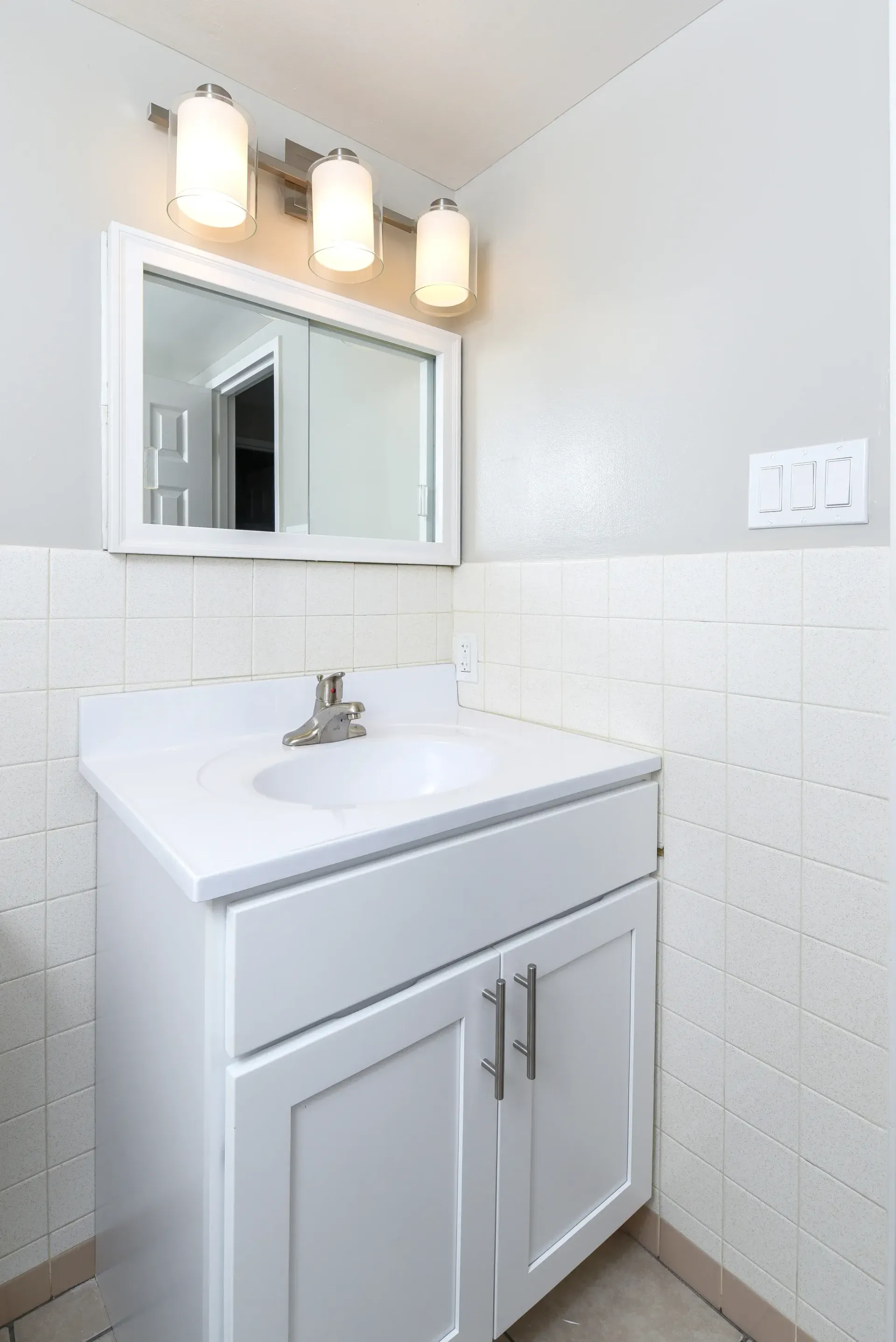 White bathroom vanity with sink, cabinet doors, and a rectangular mirror above.