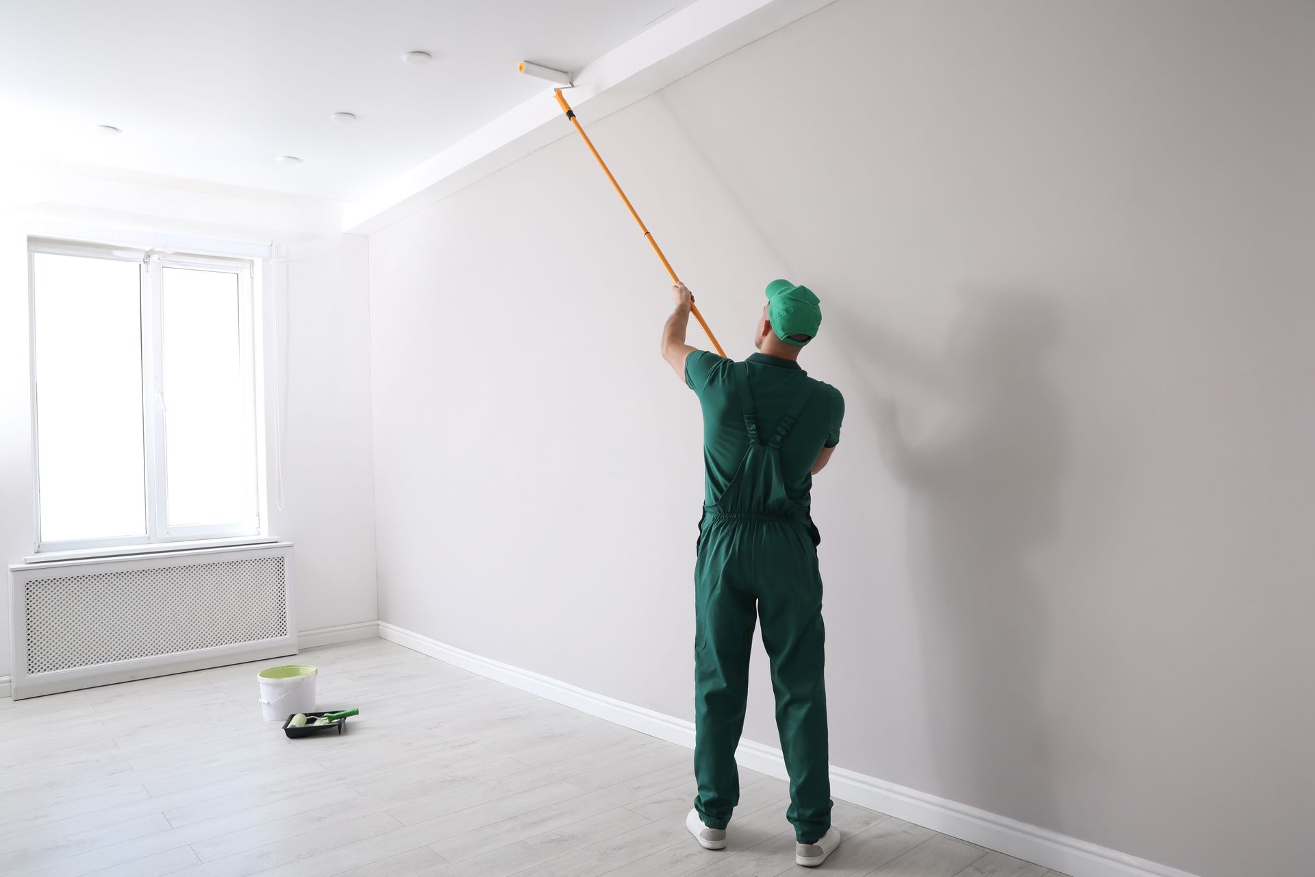 A painter is performing residential painting services, painting a ceiling with a roller in a room. A painter is performing residential painting services, painting a ceiling with a roller in a room.