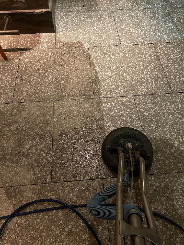 Person using a tool to clean grout lines between gray floor tiles. They wear black gloves.