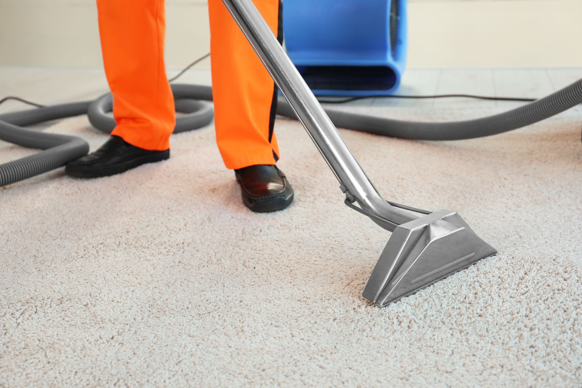Person in orange pants cleaning a white carpet with an industrial carpet cleaner.