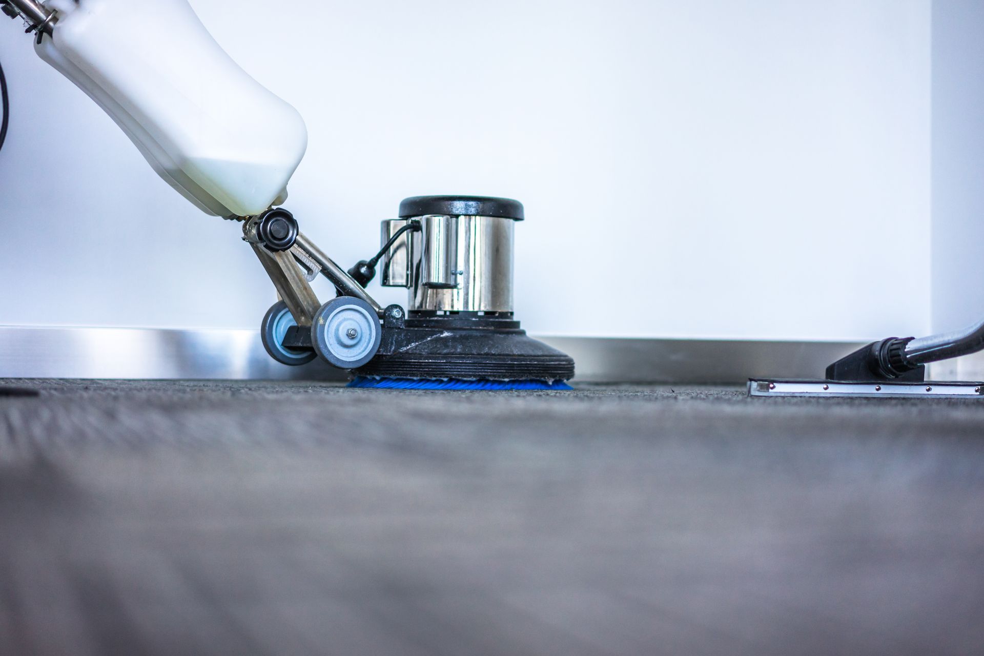 Floor buffer cleaning a gray floor next to a white wall.