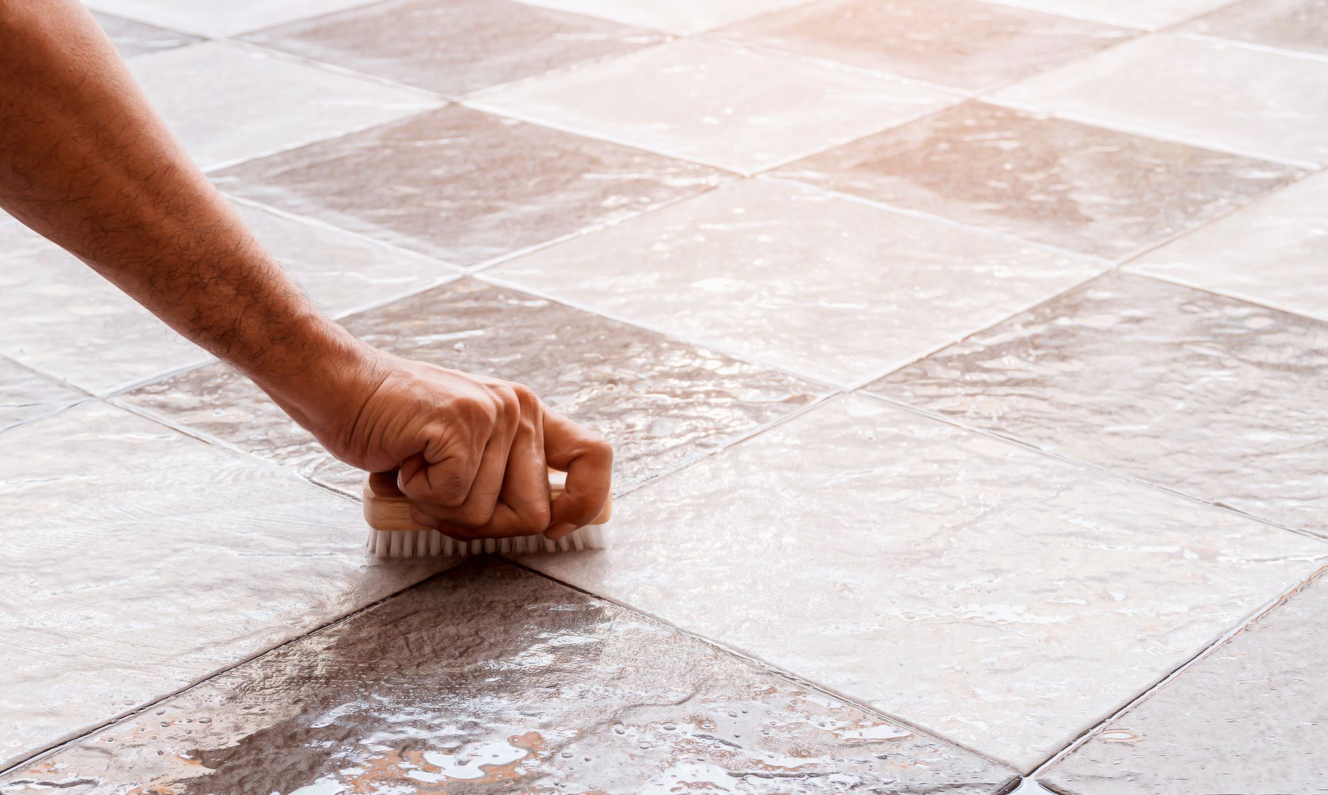 Hand scrubbing diamond-patterned floor tiles with a brush, revealing a clean surface.