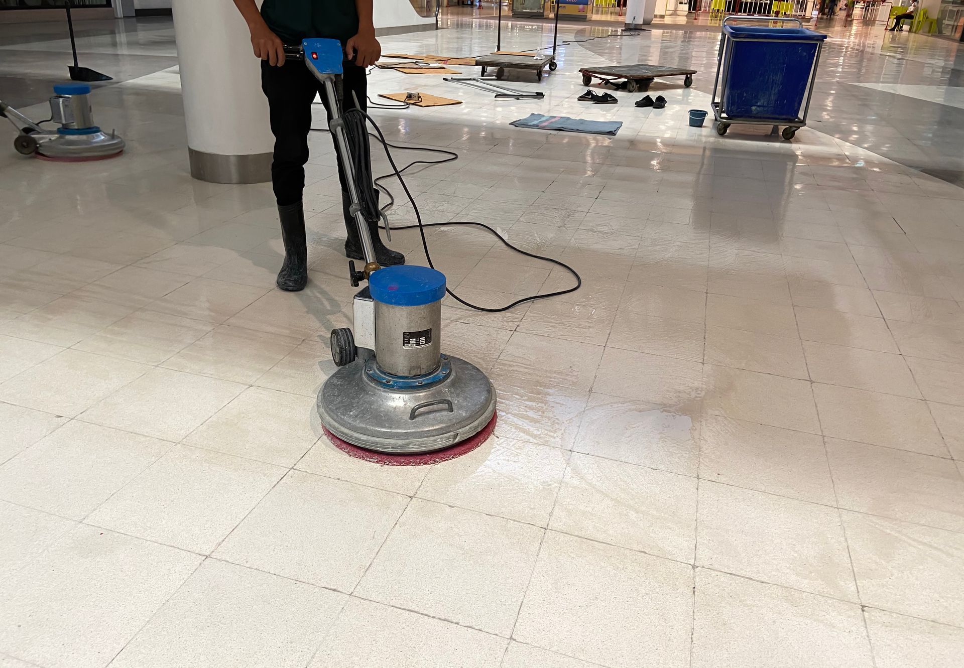 Person using a floor buffer machine in a tiled indoor area. The machine is blue and silver.