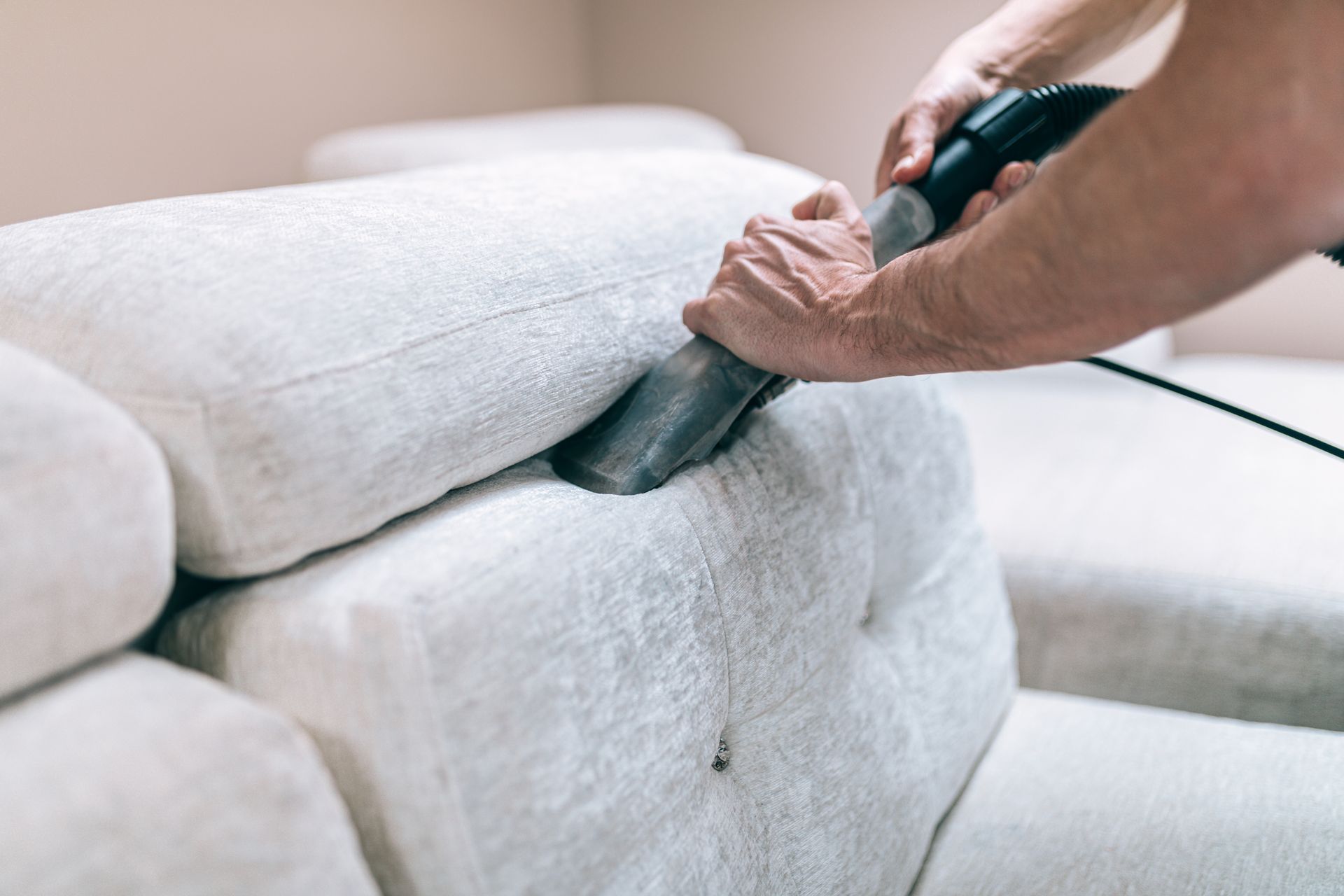 Person vacuuming a white couch, removing dirt and debris.