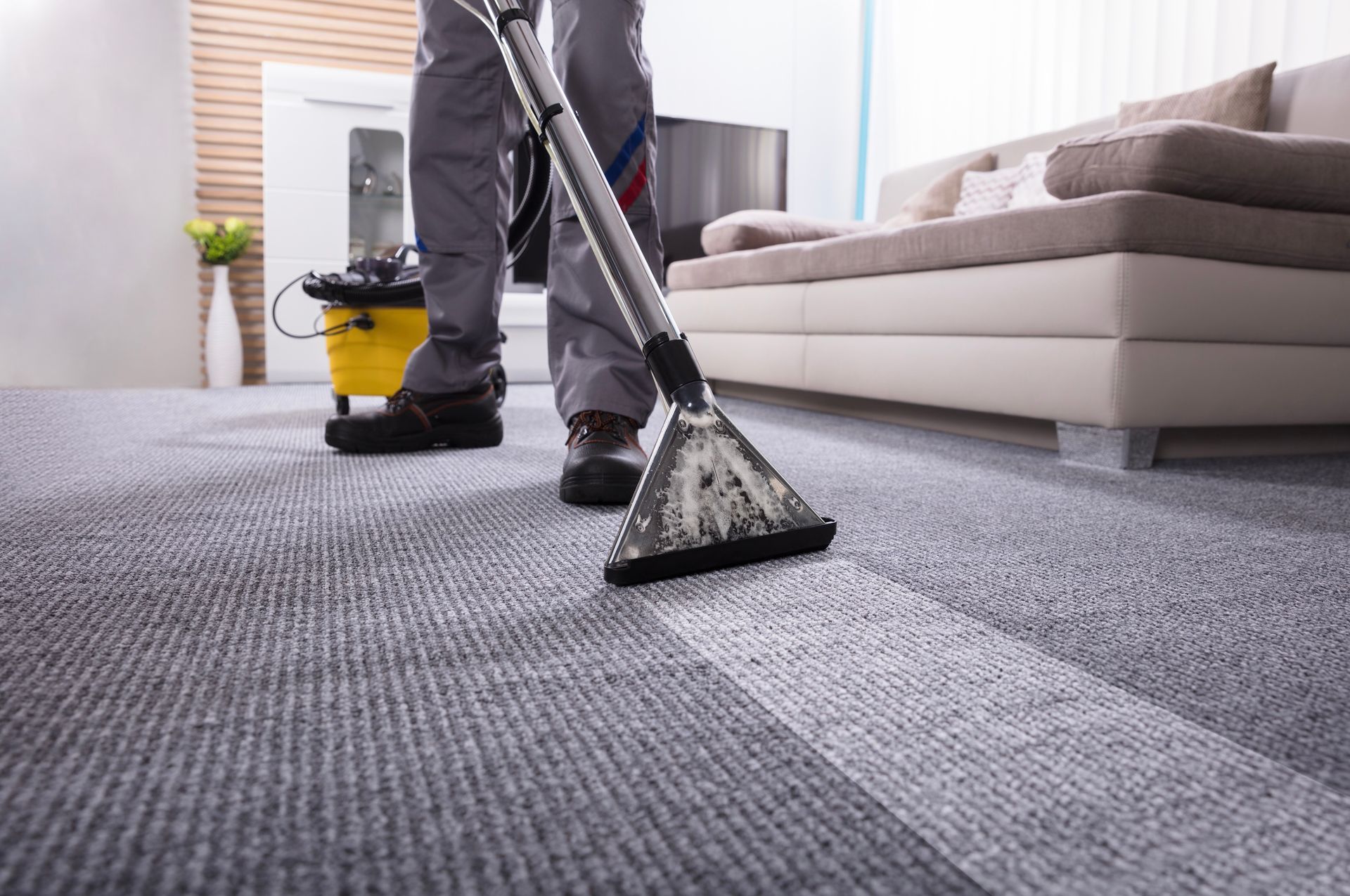 Person vacuuming a gray carpet with a cleaning machine in a living room.