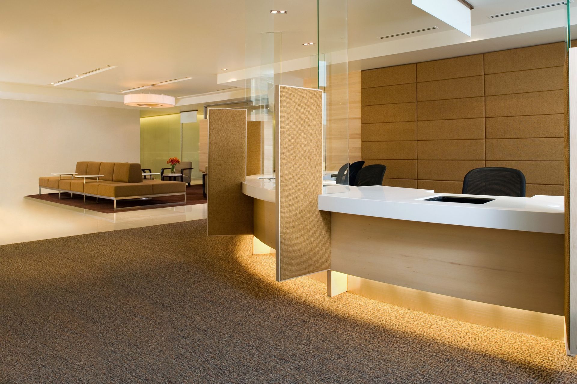 Reception area with a light wooden desk, cork panels, and a seating area in the background.