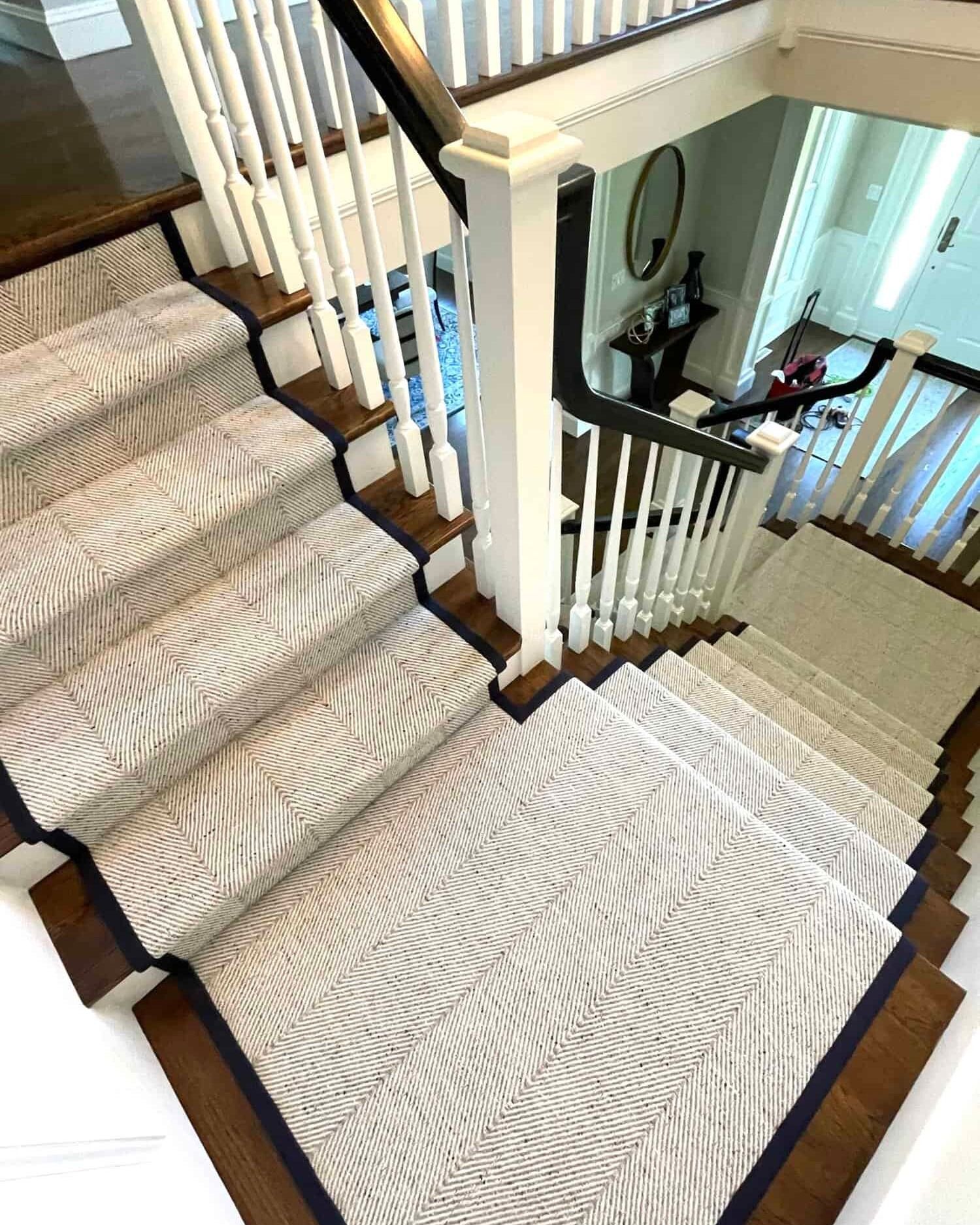 Staircase with patterned carpet and dark wood trim, leading to a hallway with a mirror and table.