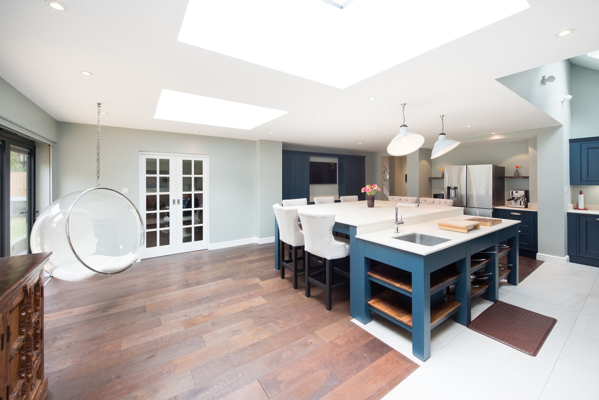 Spacious kitchen with blue island, white countertops, and hanging bubble chair; wood floors and natural light.