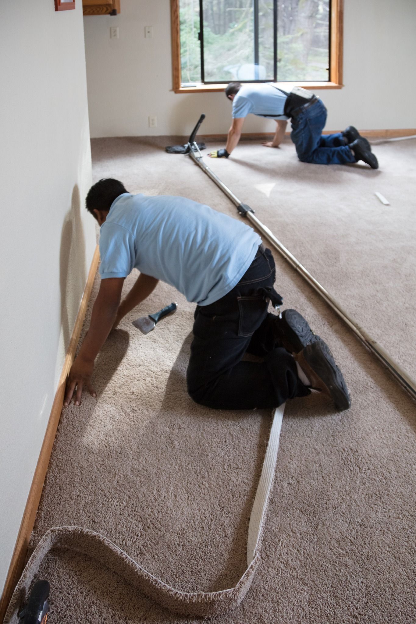 Two people installing carpet in a room, kneeling and working near the walls.