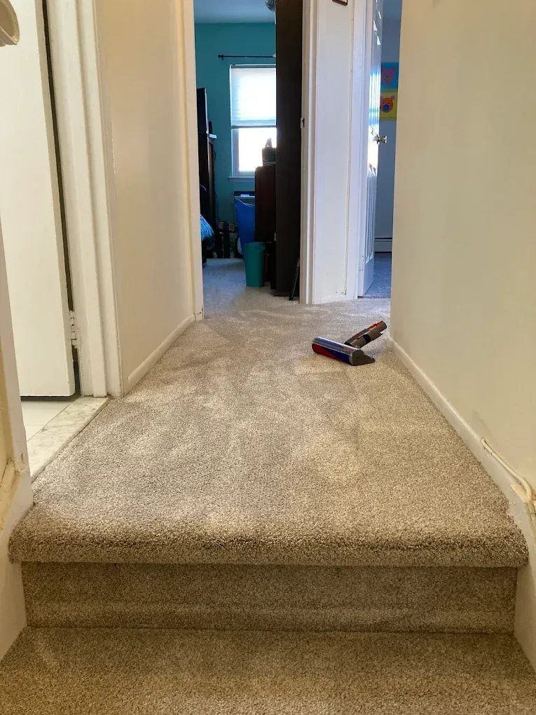 Hallway with beige carpeted stairs. A cordless vacuum rests on the carpet.