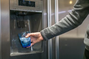 a person is pouring ice into a glass of water from a refrigerator