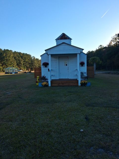 A small, white, chapel-style building with a steeple and wooden steps, set in a sunny, grassy field.
