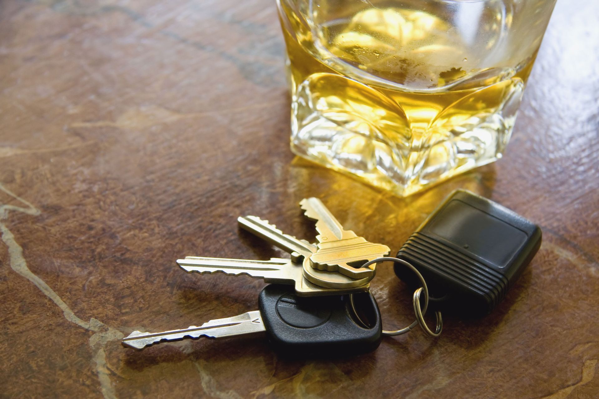 Whiskey in a glass next to car keys, likely representing drunk driving.