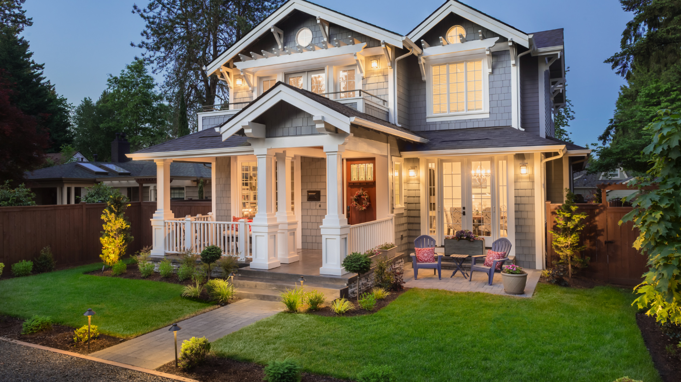 Two-story gray house with white trim, porch, and manicured lawn. Evening lighting.
