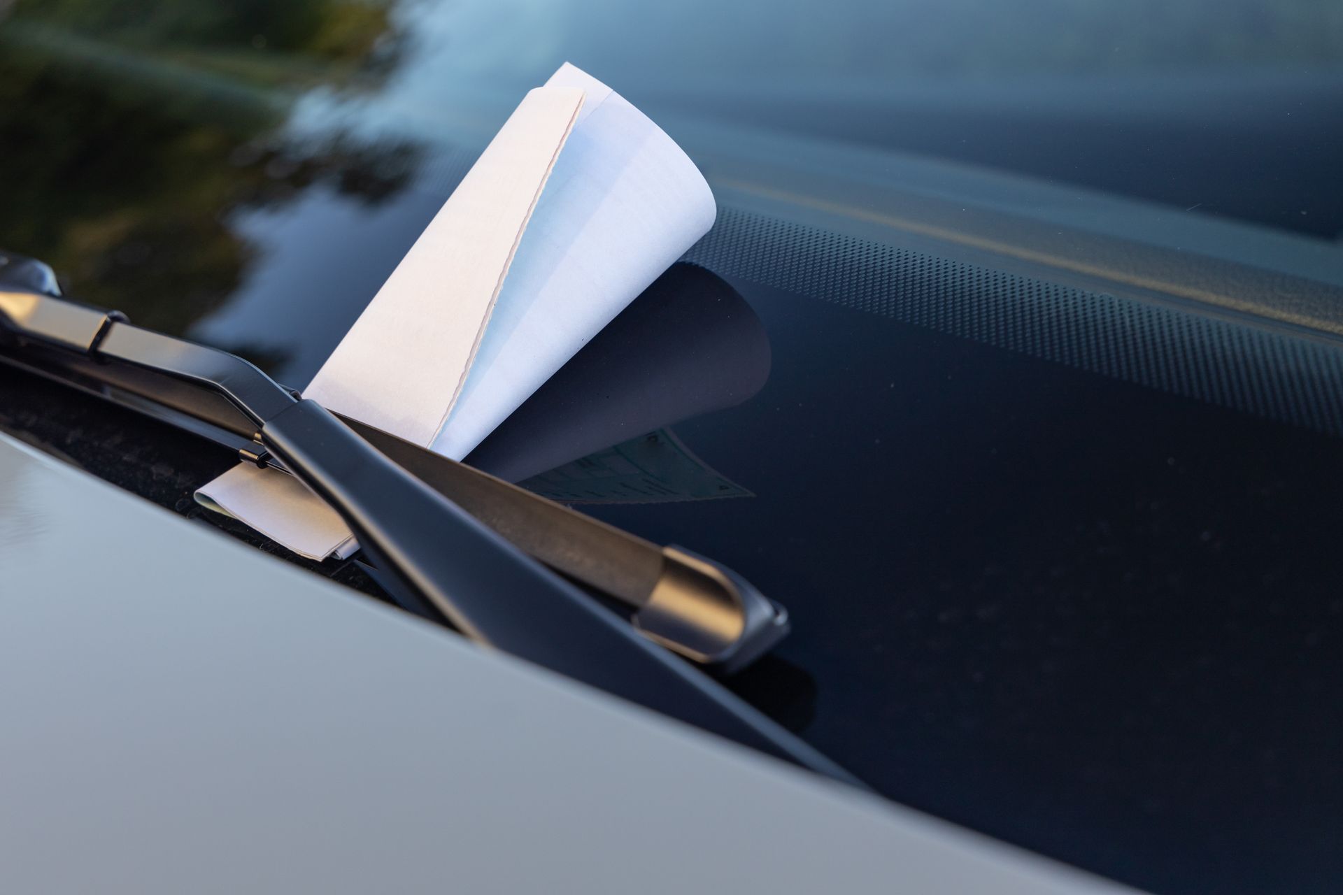 Paper notice tucked under a windshield wiper, indicating a parking ticket. Paper notice tucked under a windshield wiper, indicating a parking ticket.