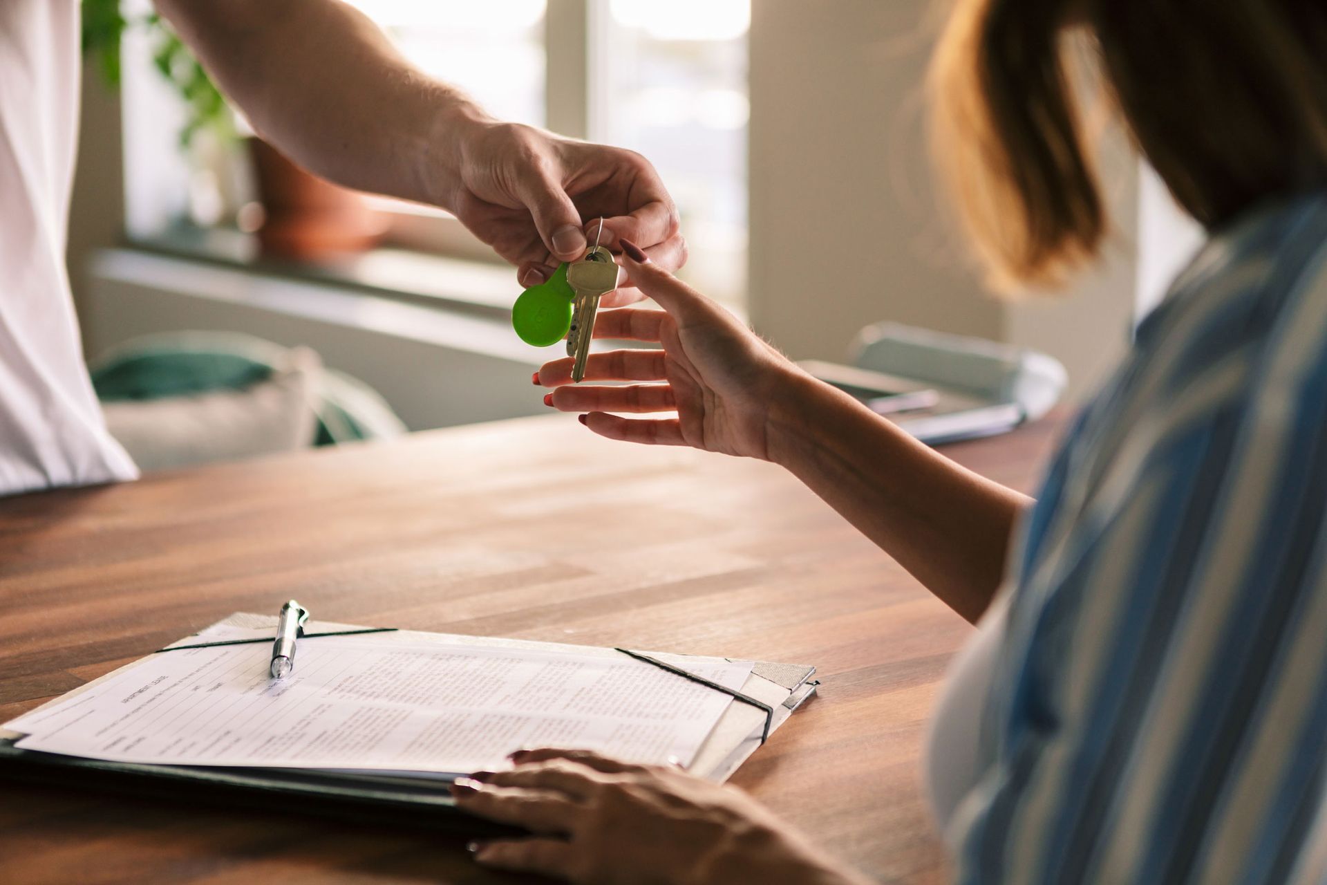 Person handing keys to another person at a desk over paperwork.