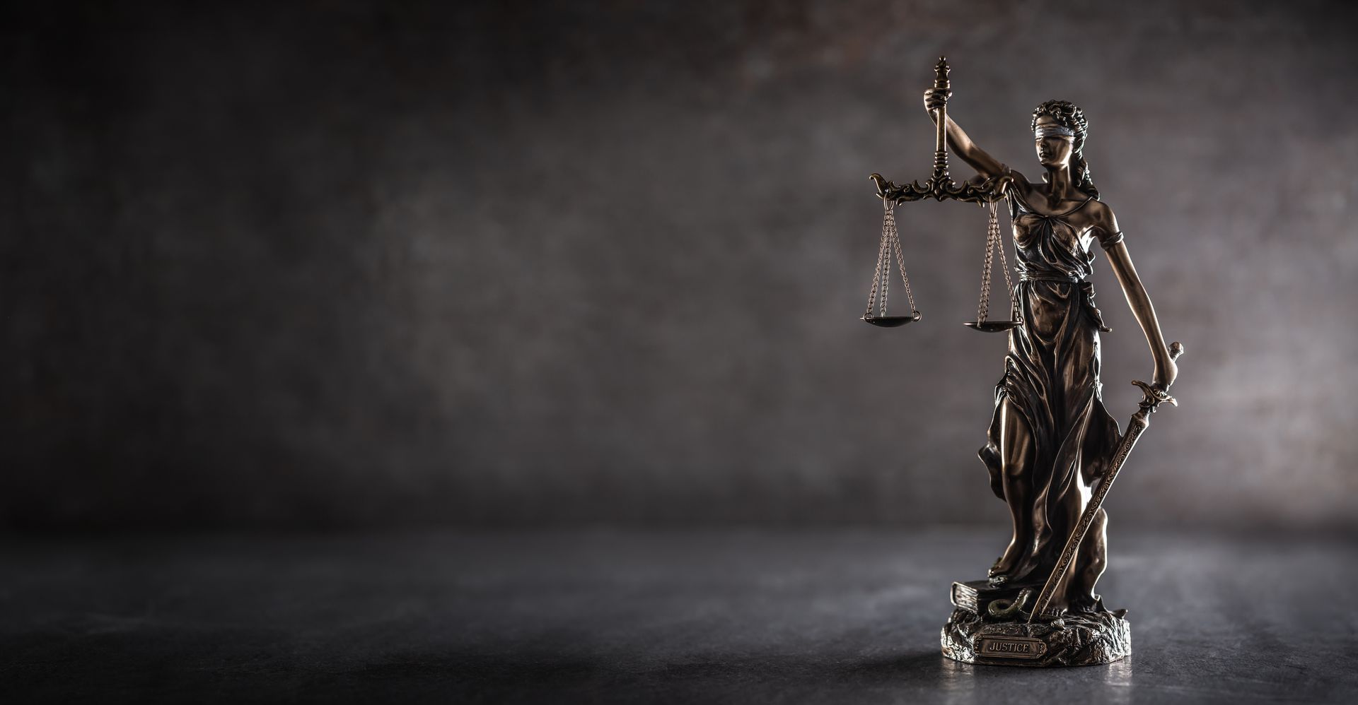Statue of Lady Justice, holding scales, on a textured dark background.