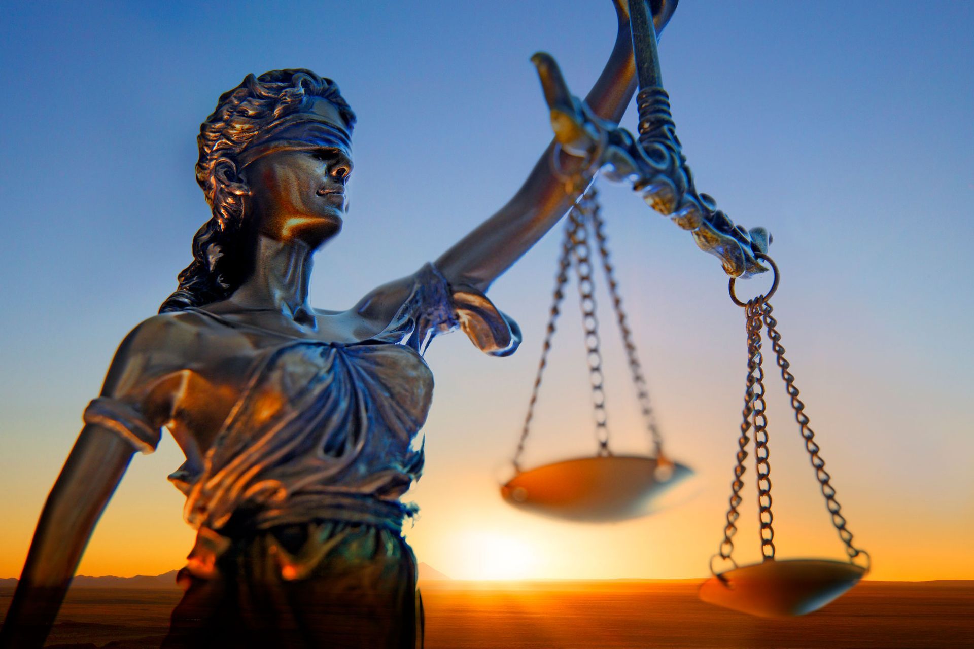 Statue of Lady Justice with blindfold, scales, and sunset background.